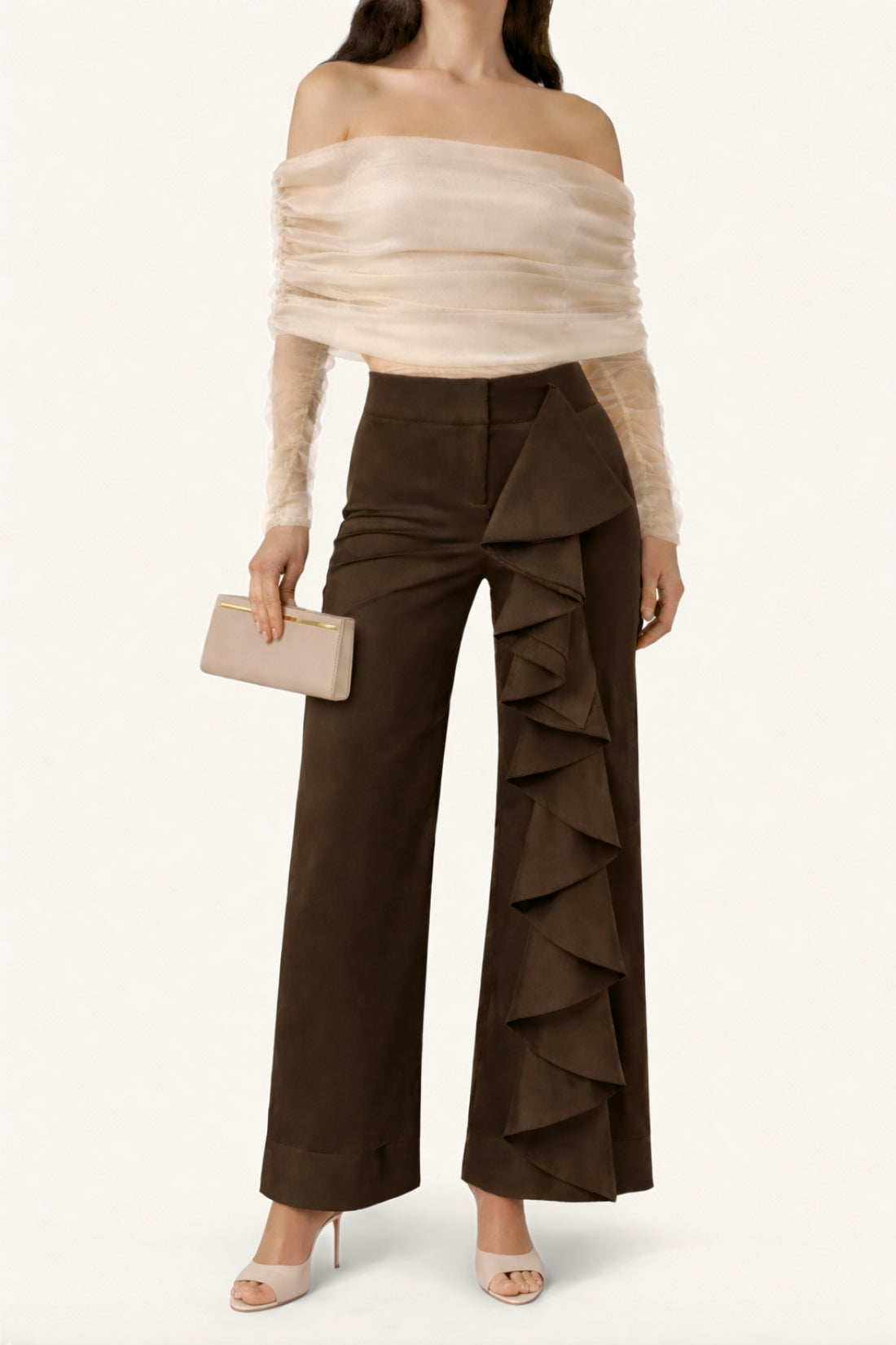 Woman wearing a beige off-shoulder top and brown ruffled pants on a white background