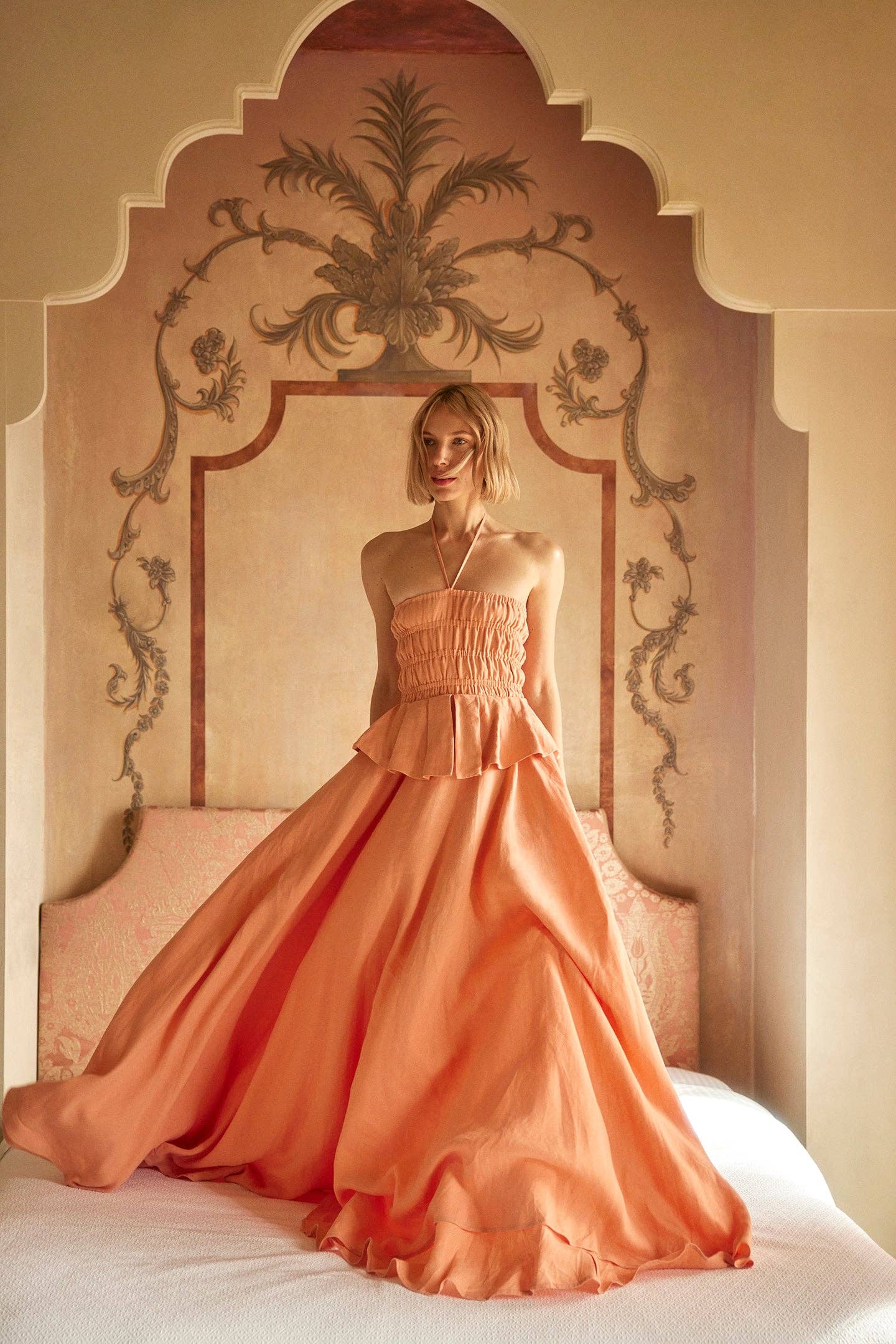Woman in a peach-colored gown standing in an ornate room.