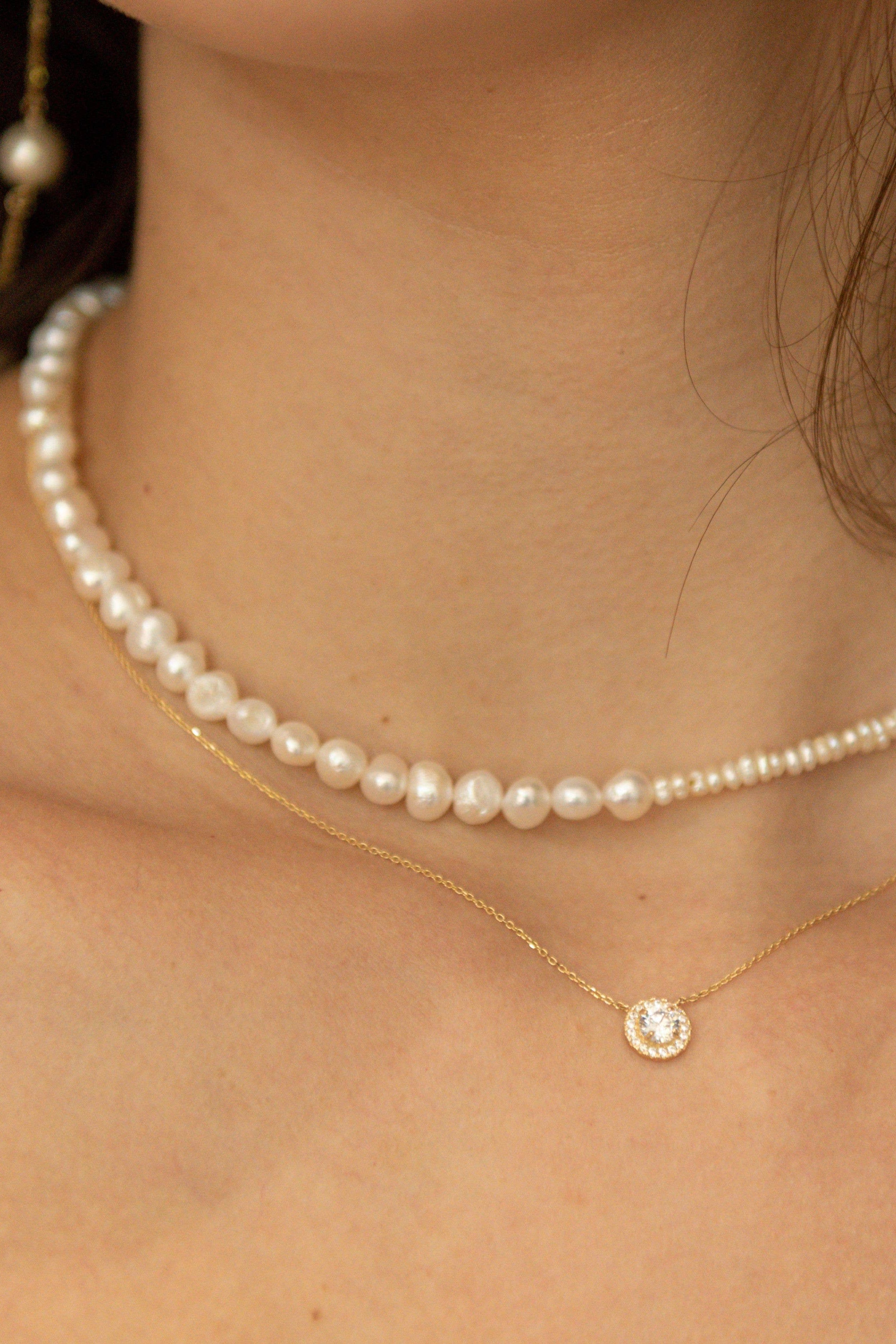 Close-up of a pearl necklace and gold chain with a small round pendant.