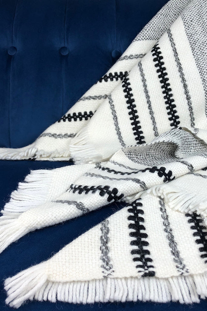 White blanket with black and gray stripes and tassels on a blue surface