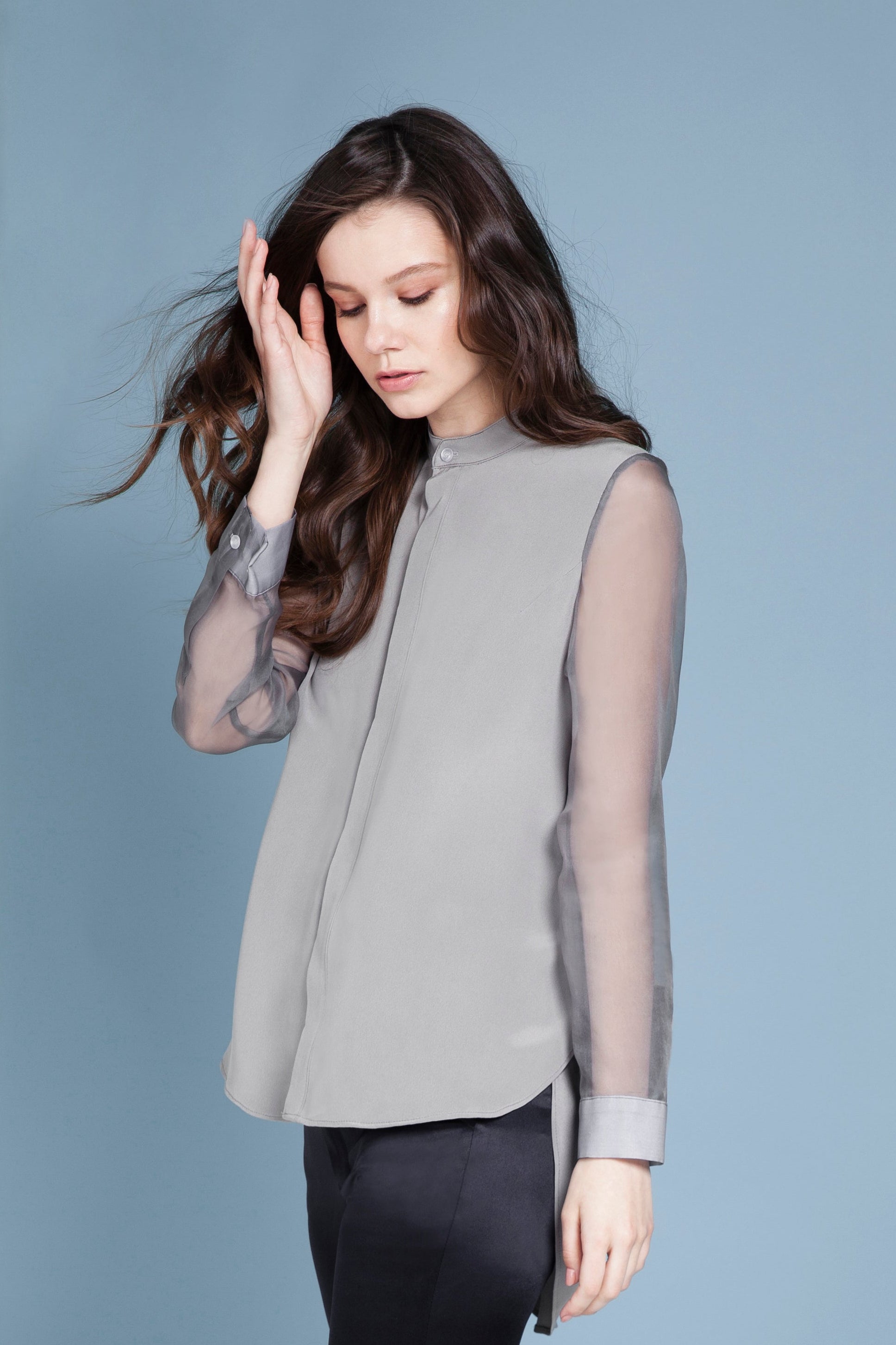 Woman wearing a sheer long sleeved silk gray top with sheer sleeves against a blue background