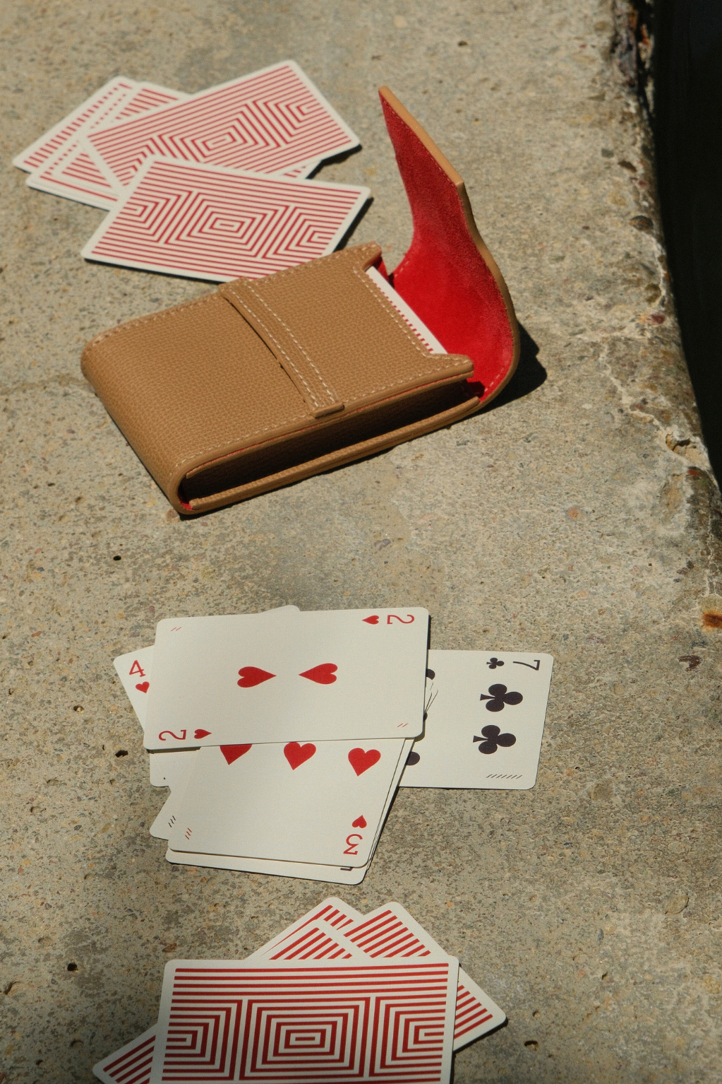 Playing cards and a brown wallet on a concrete surface