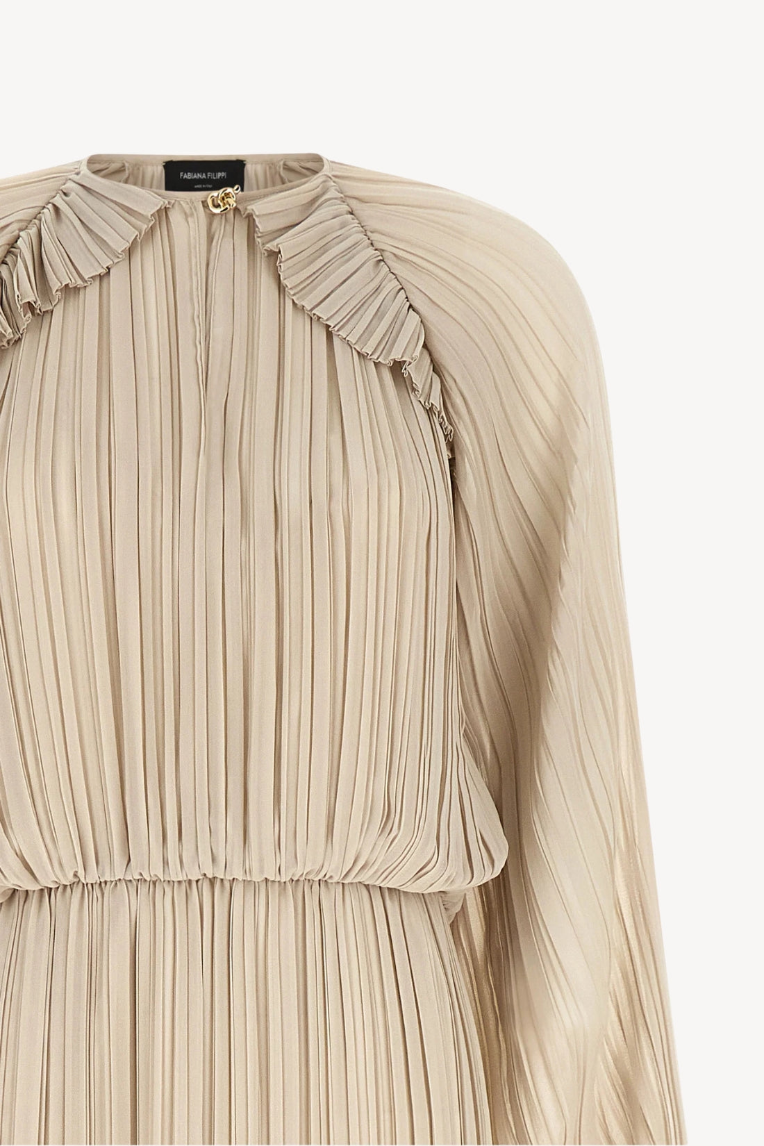 Close-up of a pleated long-sleeve top in a light beige or cream color, featuring a ruffled collar and a small gold button at the neckline.