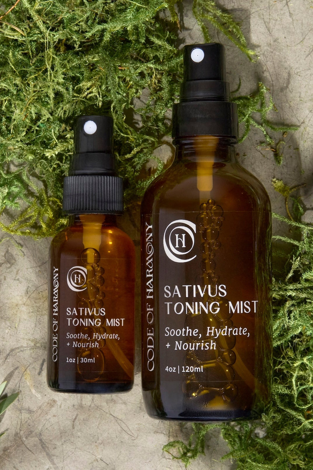 Two bottles of Code of Harmony Sativus Toning Mist on a textured surface with greenery.