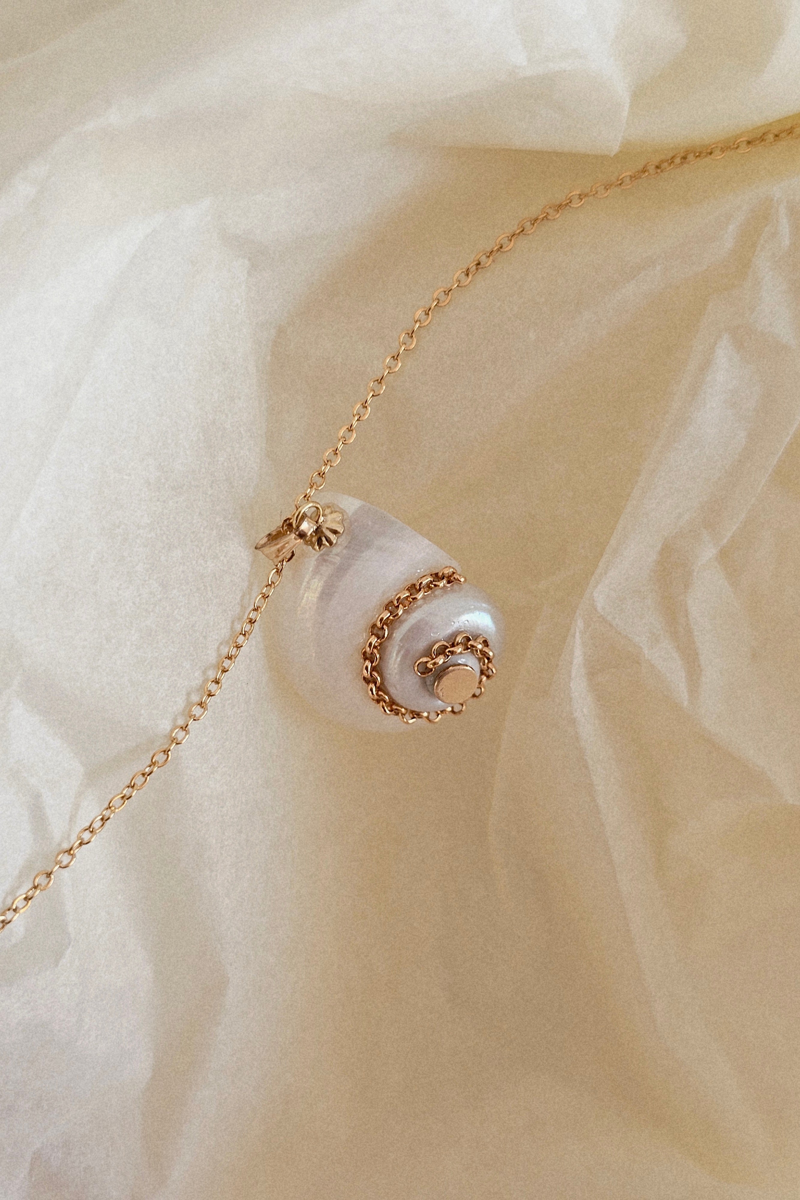 Gold necklace with a pearl pendant on a soft beige fabric background