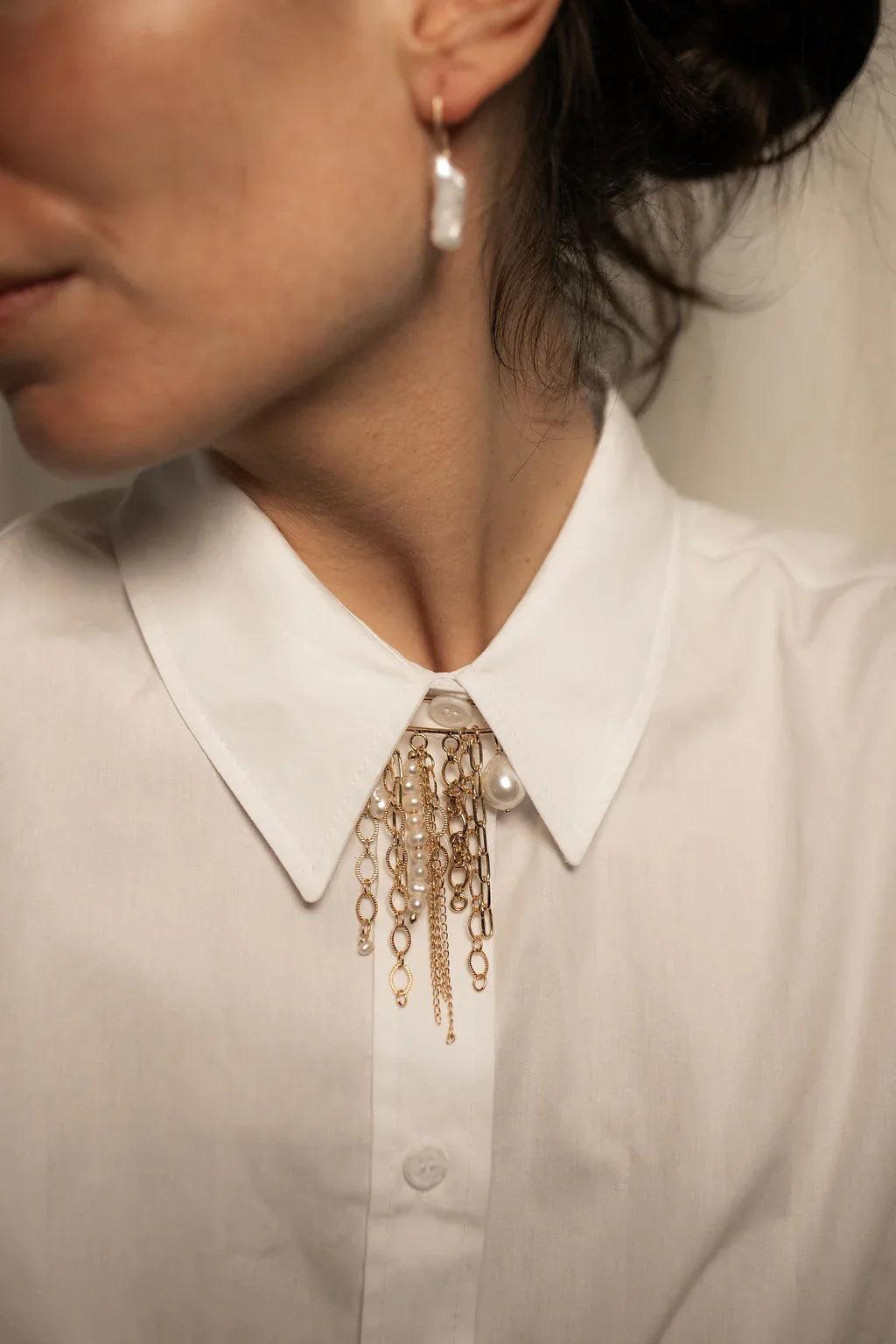 Close-up of a person wearing a white shirt with gold chain accessories and a pearl earring.