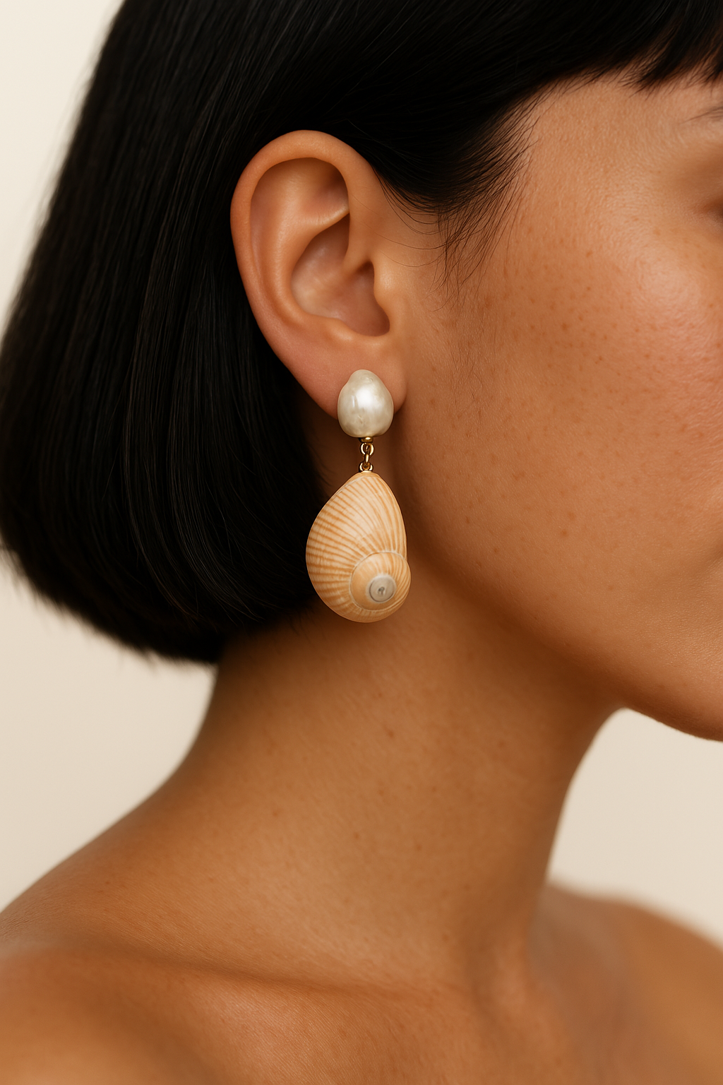 Close-up of a person wearing a shell and pearl earring against a neutral background