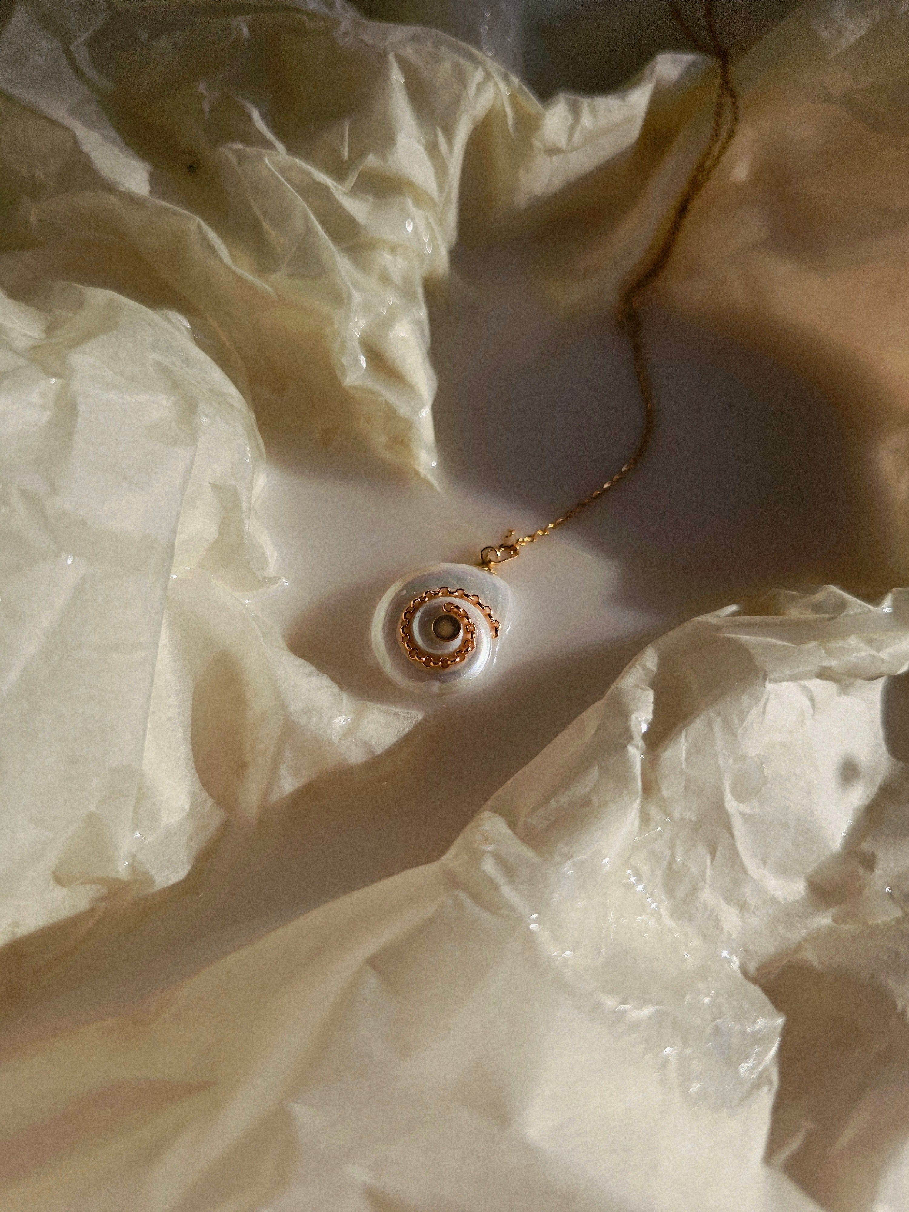 Gold necklace with a spiral pendant on a textured beige surface