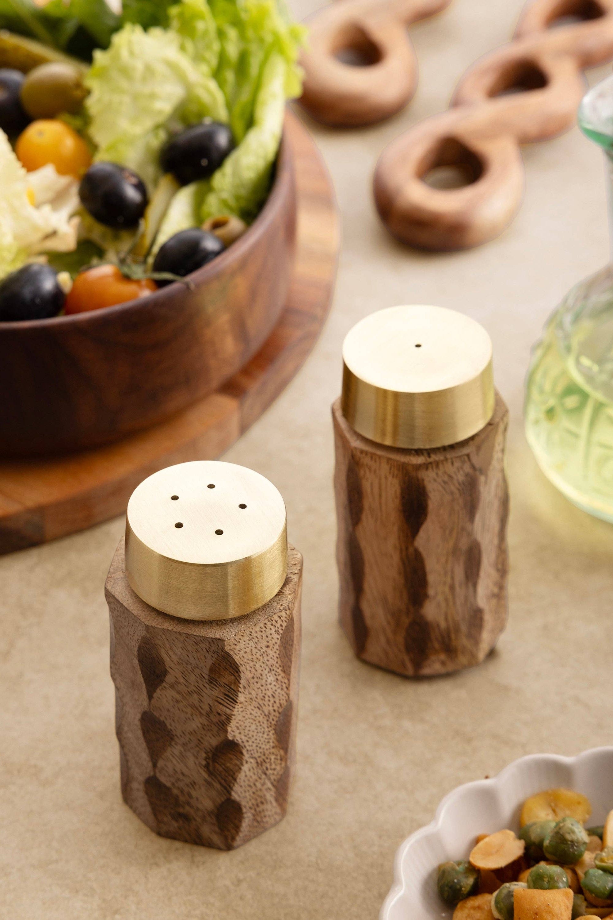 Wooden salt and pepper shakers on a table with a salad and bread in the background