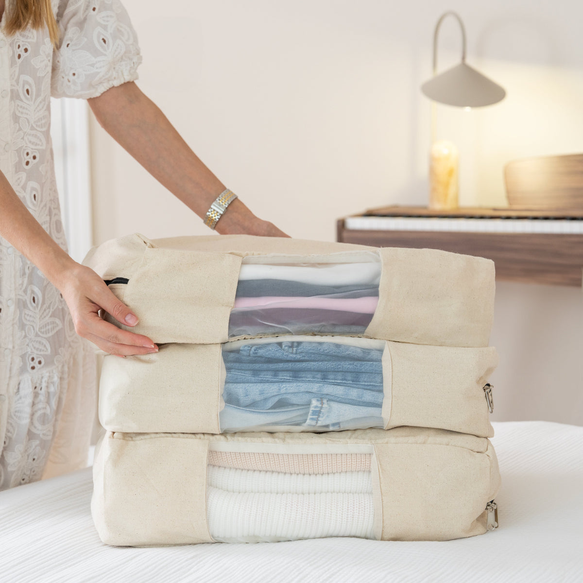 Person holding a folded garment in a beige packing cube on a bed.