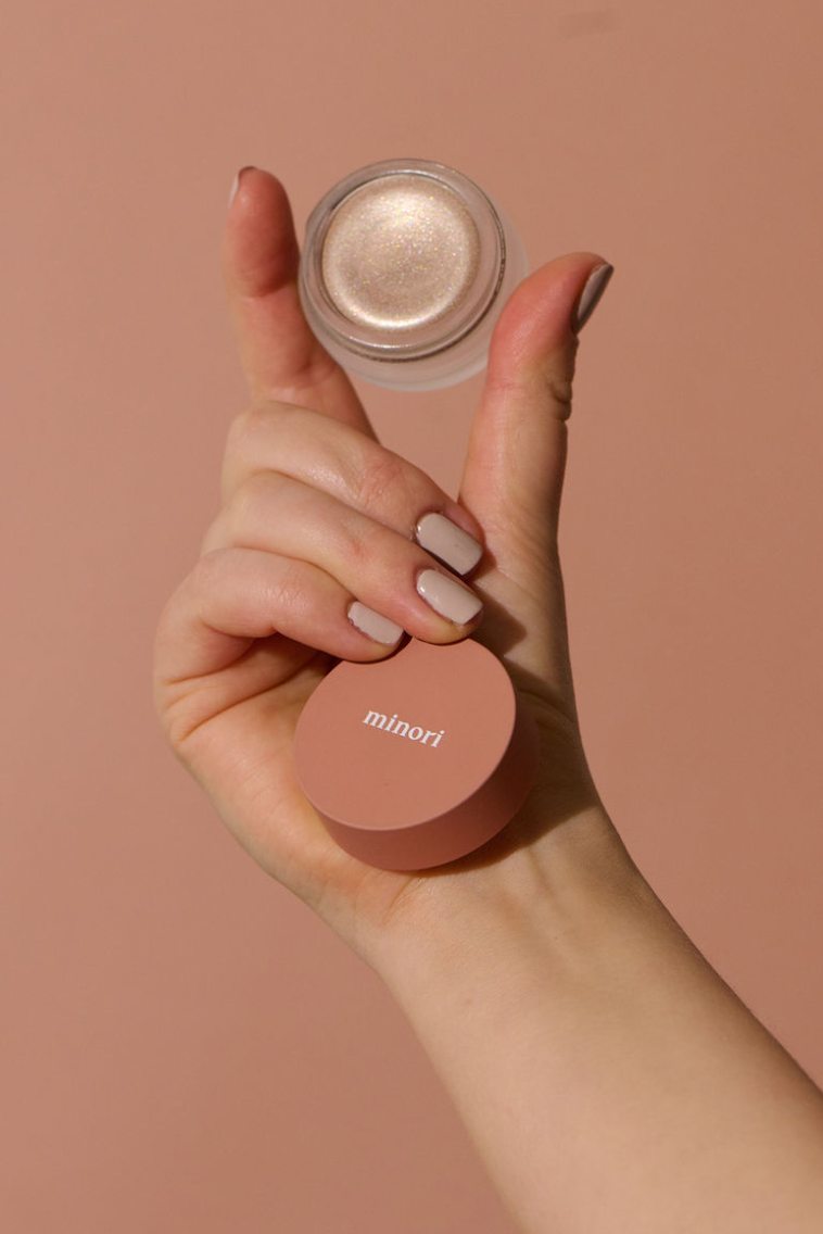 Hand holding up shimmering face highlighter makeup.