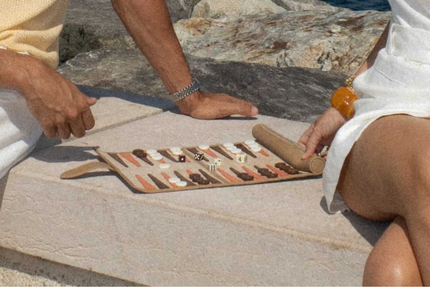 Two people playing backgammon on a stone surface outdoors.