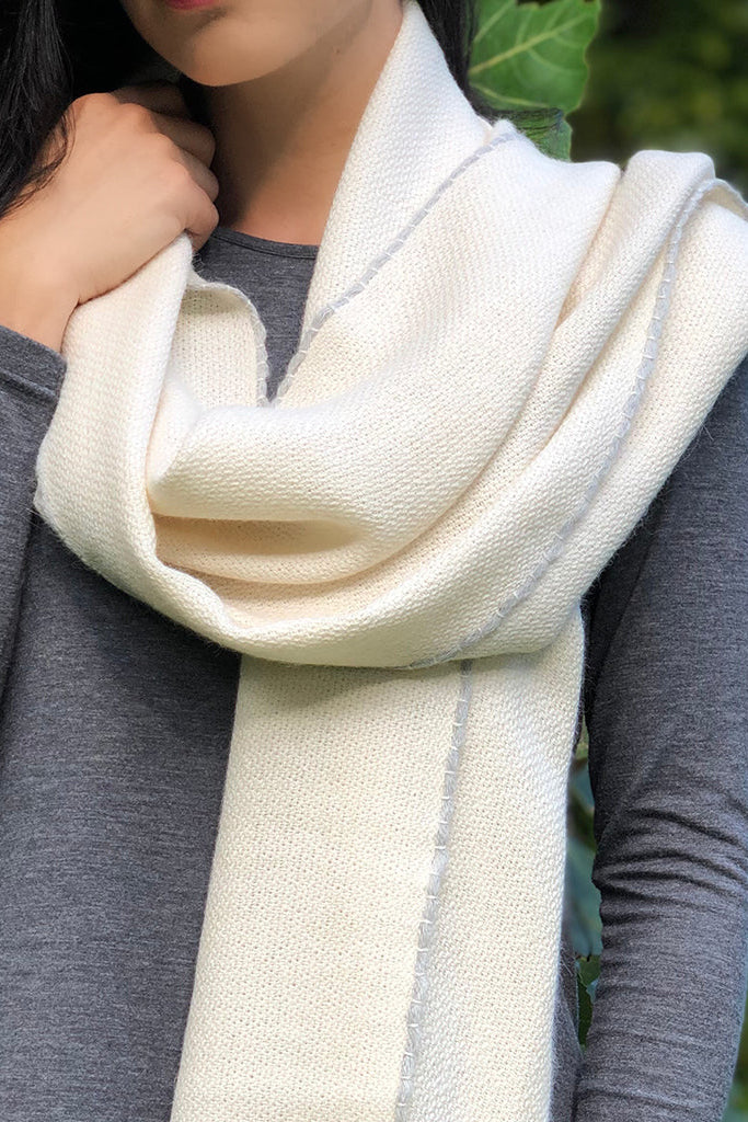 Person wearing a cream scarf with a blurred green leafy background