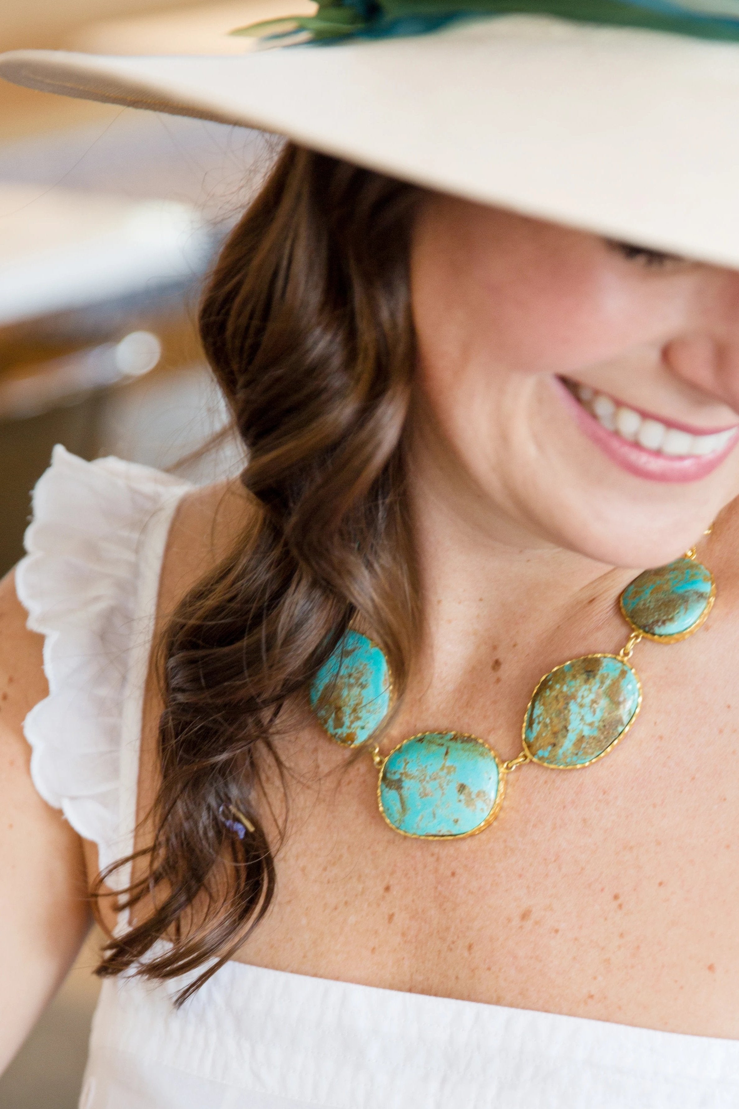Woman wearing a white hat and white top with turquoise jewelry