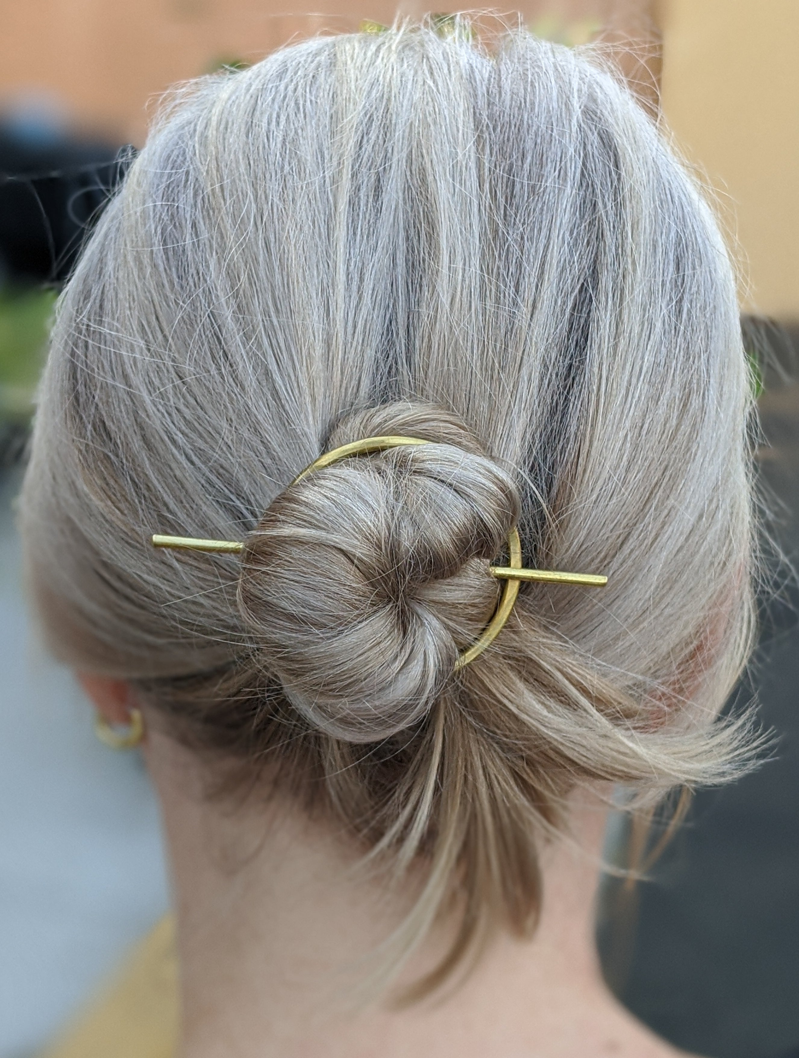 Close-up of a person's hair styled in an updo with a hairpin, blurred background