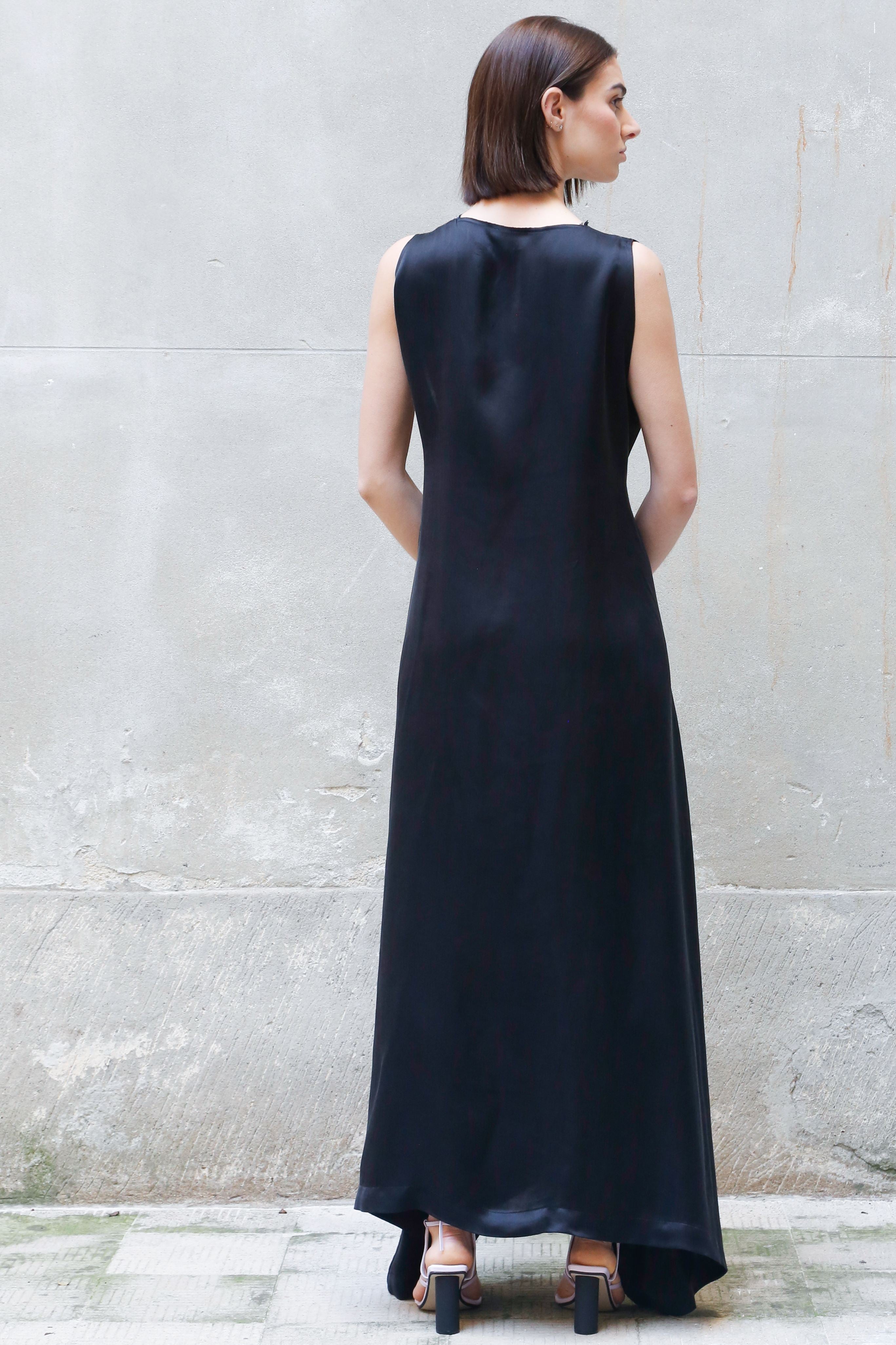 Woman wearing a black sleeveless dress standing against a gray wall.