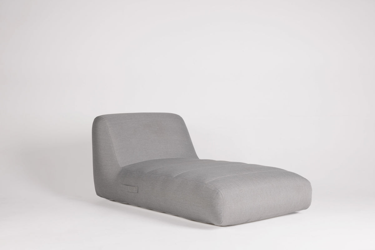 A modern low-profile chaise lounge chair upholstered in light gray fabric, shown against a seamless light gray studio background.
