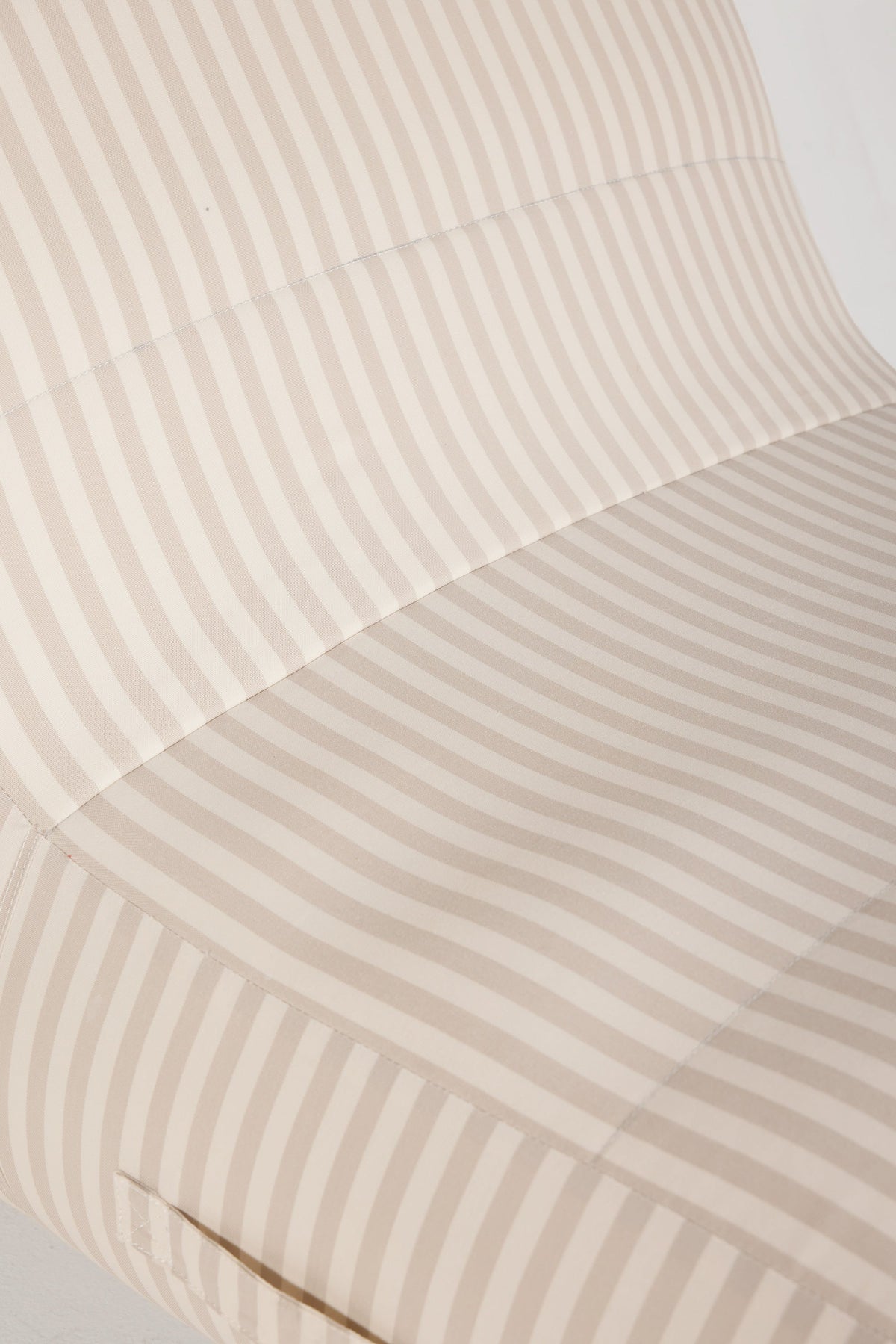 Close-up of a striped fabric surface in warm beige and off-white tones, showing the texture and pattern of the material.