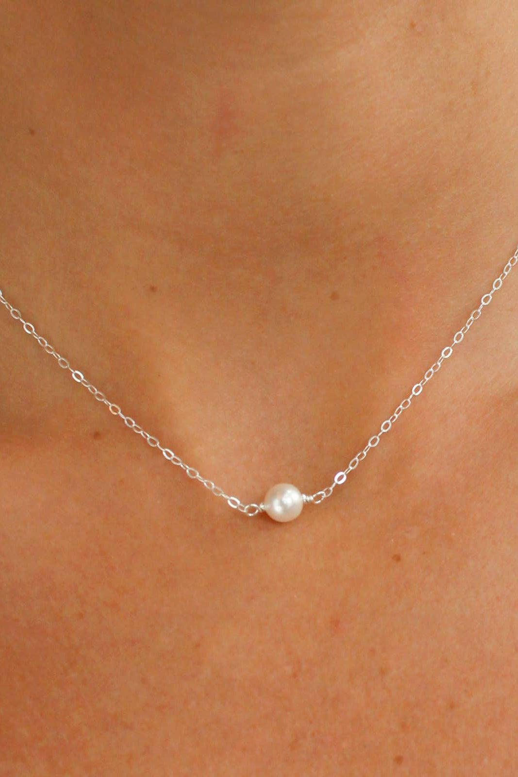 A sterling silver necklace with a single pearl solitaire on a minimalistic chain, worn by a person.