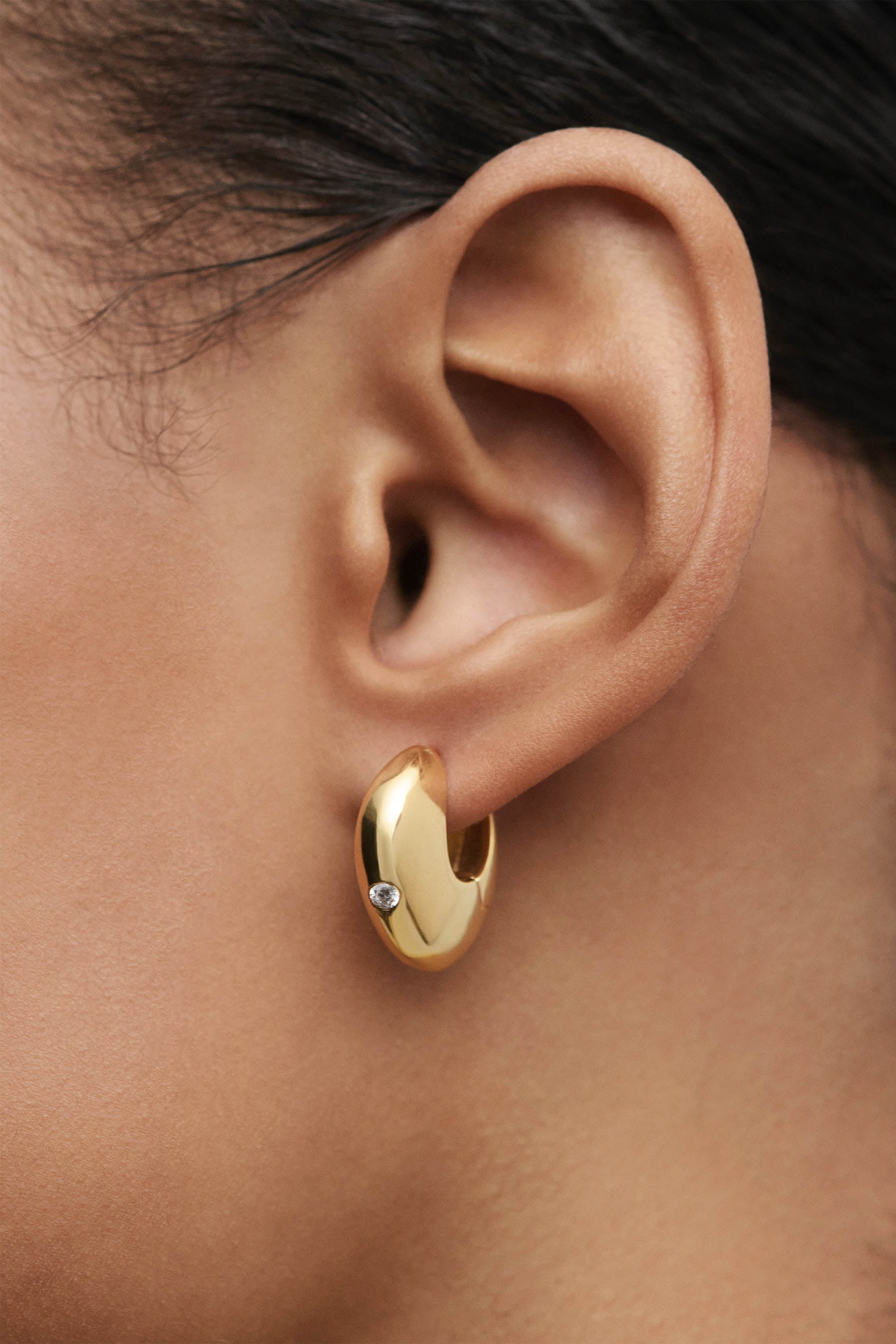 Gold hoop earring worn by a person with dark hair.