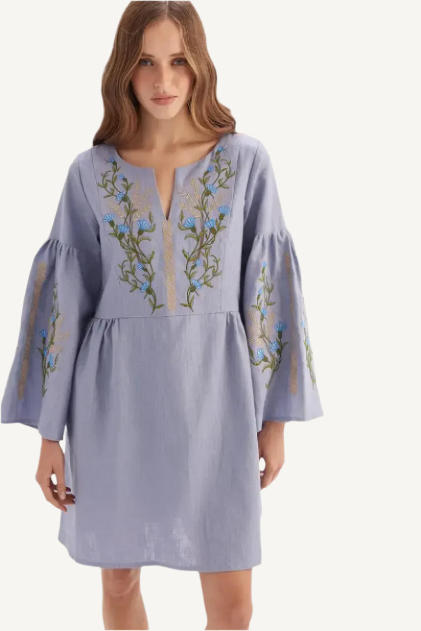 A woman wearing a lilac linen embroidered dress with floral accents.
