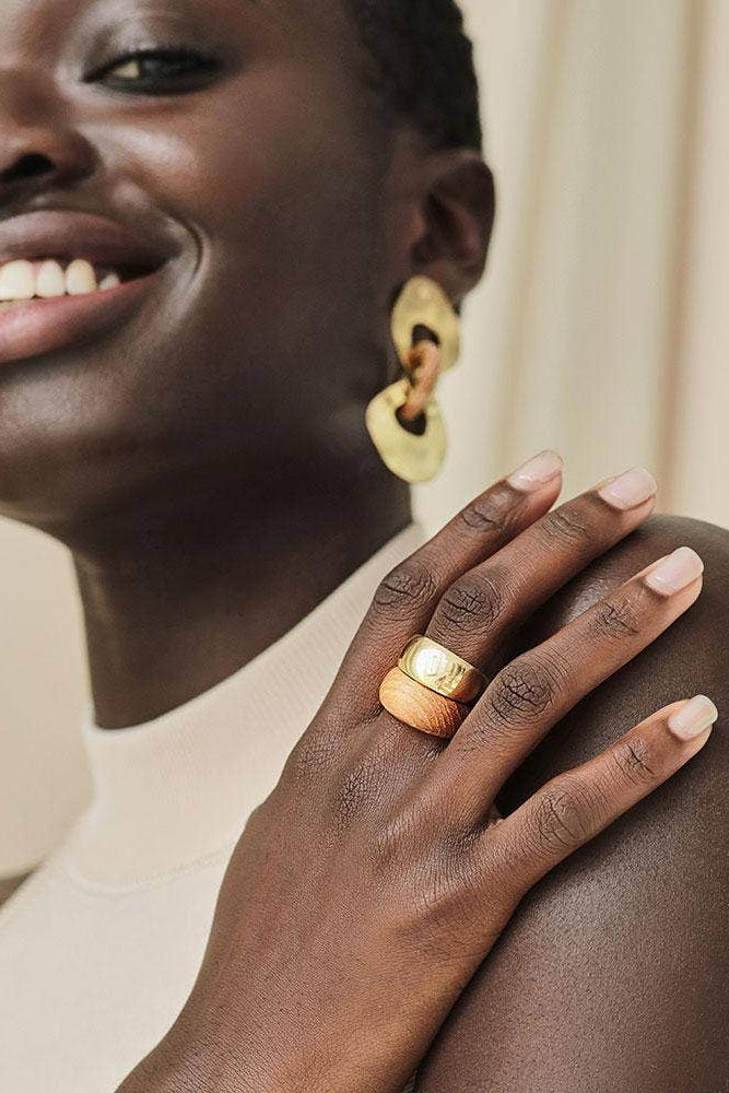 Woman wearing gold earrings and ring, smiling with hand on shoulder