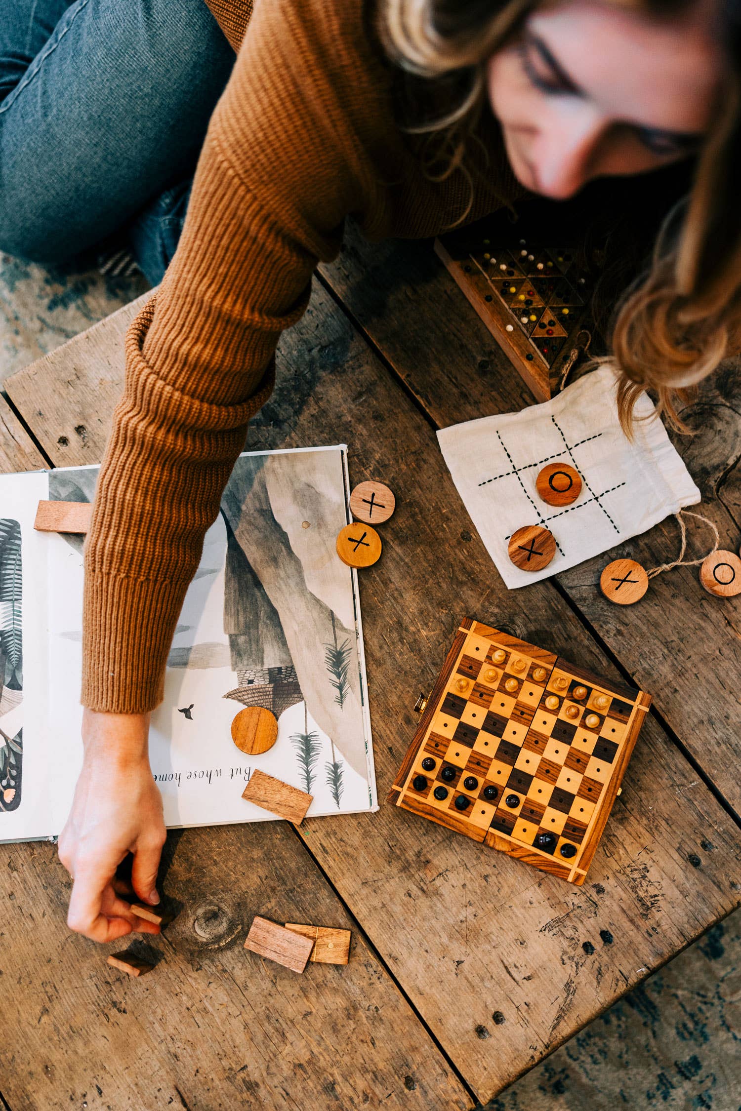 Person playing a wooden checkers game on a rustic wooden table.