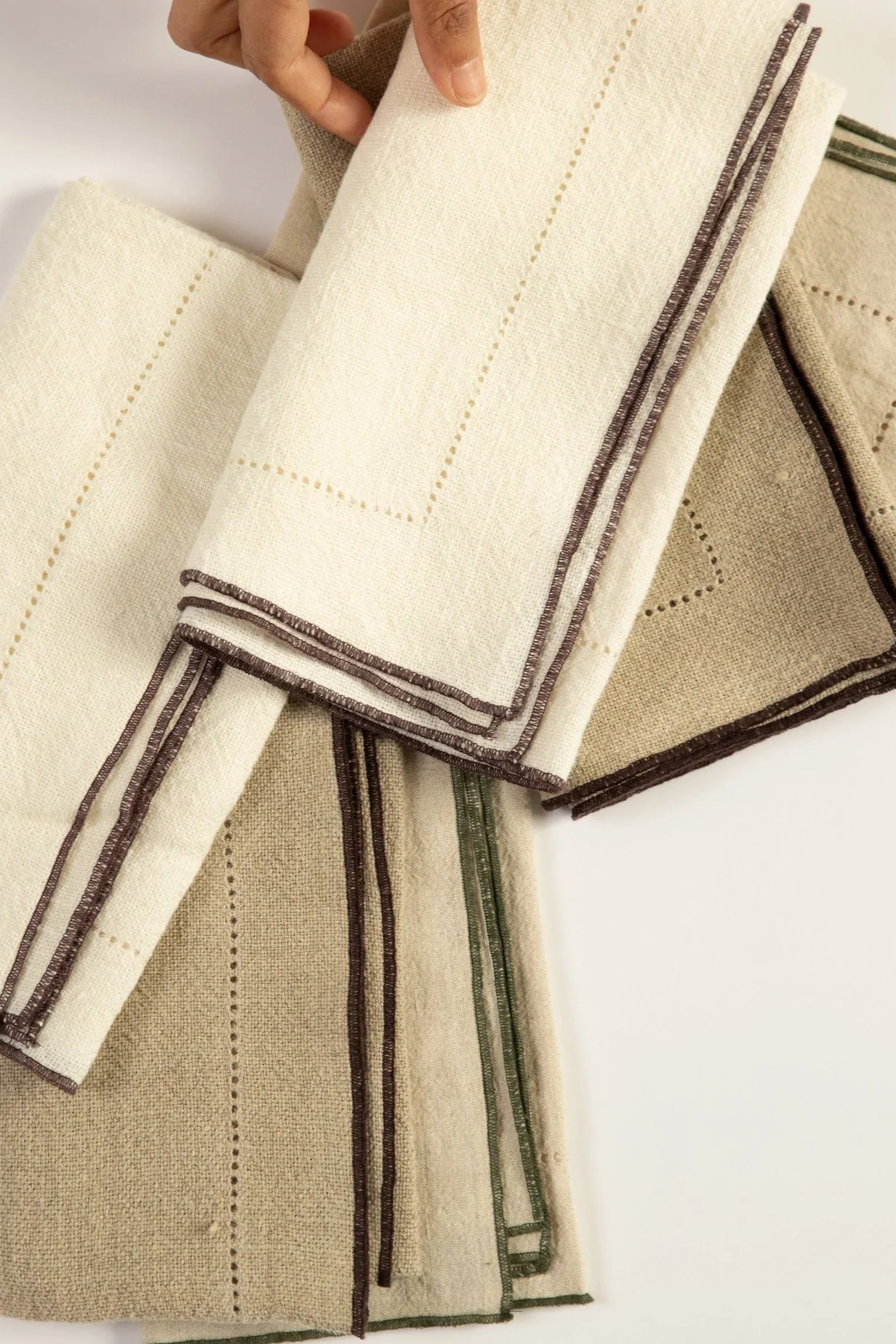 Set of folded fabric napkins with brown trim on a white background