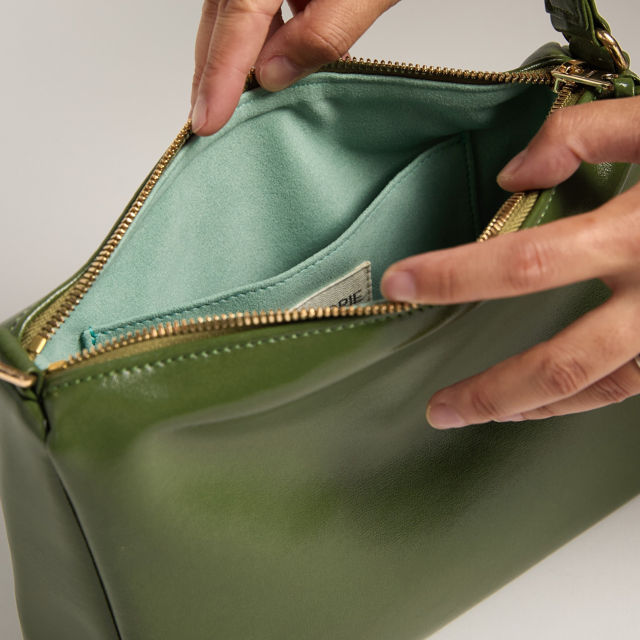 Green handbag with a gold zipper being opened by a hand.