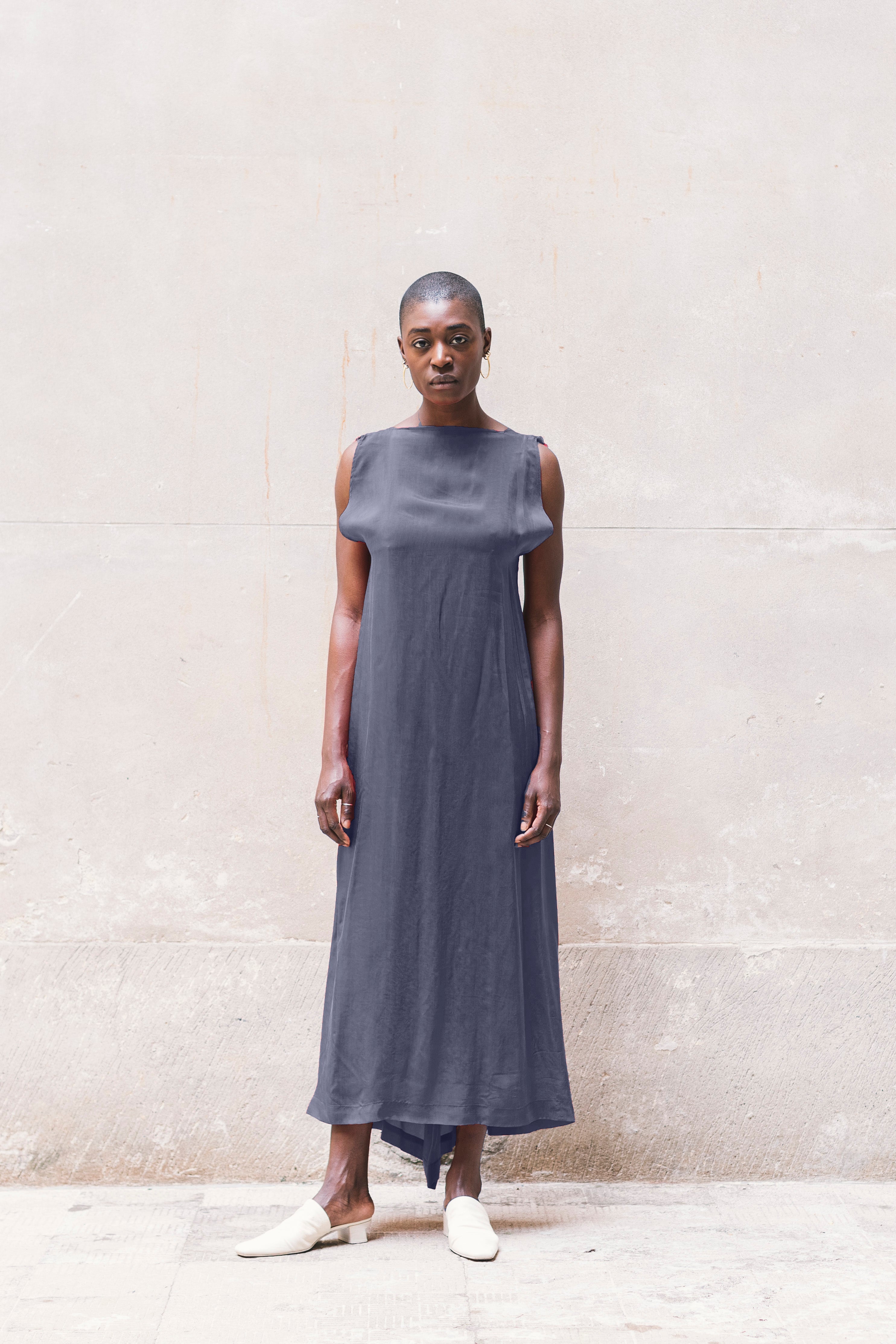 Woman wearing a long dark blue dress against a light gray wall.