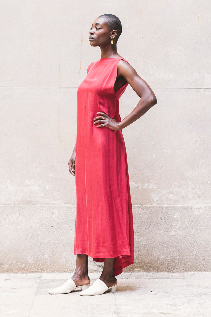 Woman wearing a red dress standing against a light-colored wall.