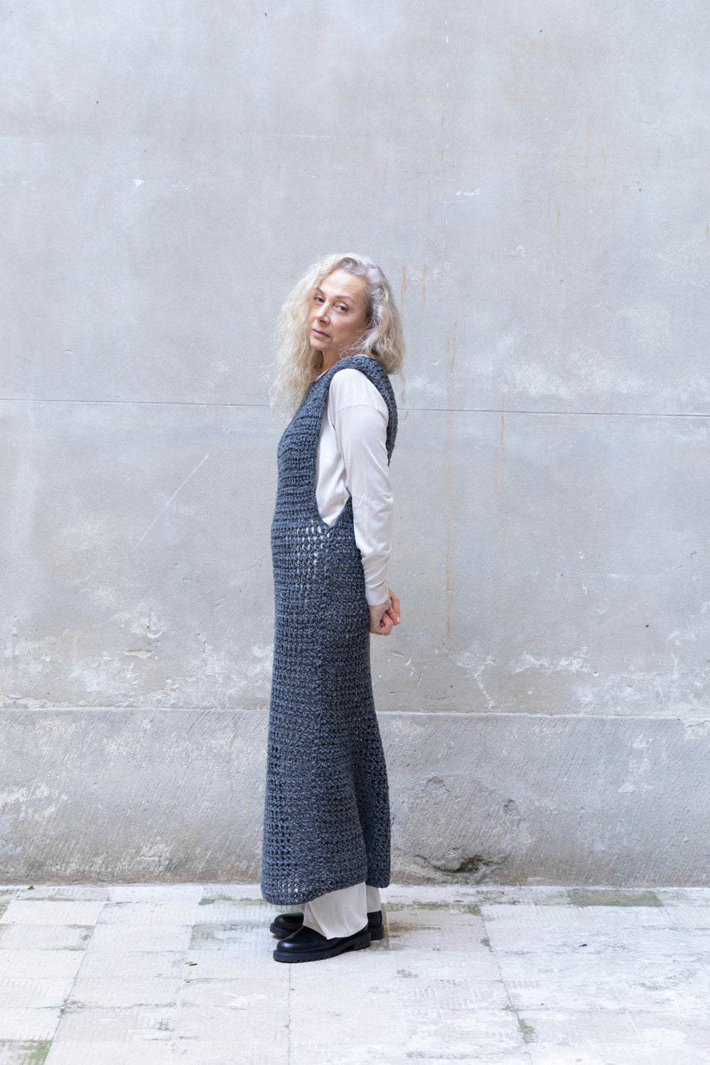 Woman wearing a long knitted dress against a gray wall