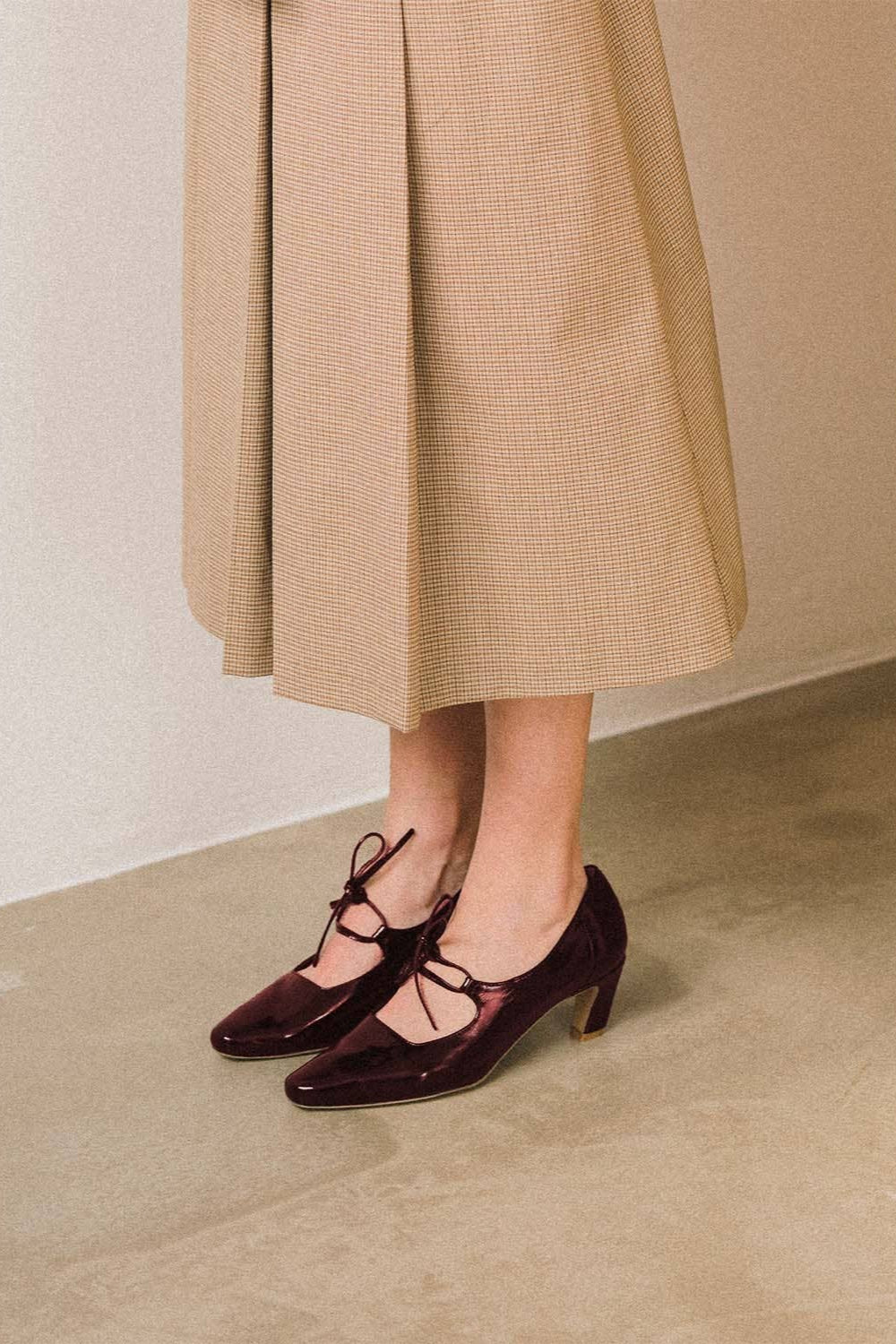 Person wearing a beige coat and dark shoes on a neutral background