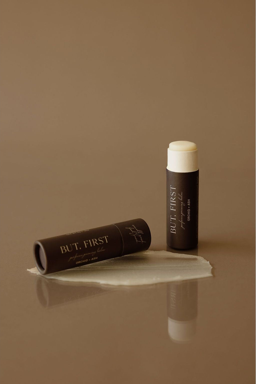 BUT FIRST lip balm and packaging on a brown background