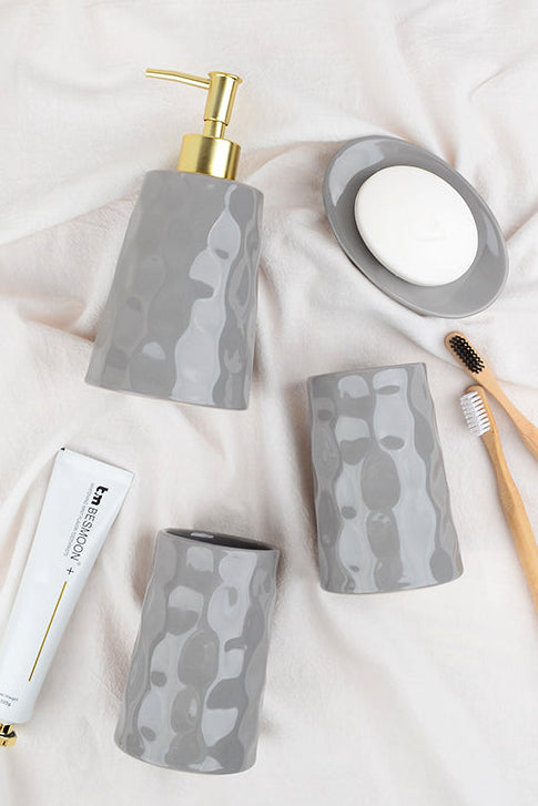 Bathroom accessories including a soap dispenser, toothbrush holder, and containers on a light fabric background.
