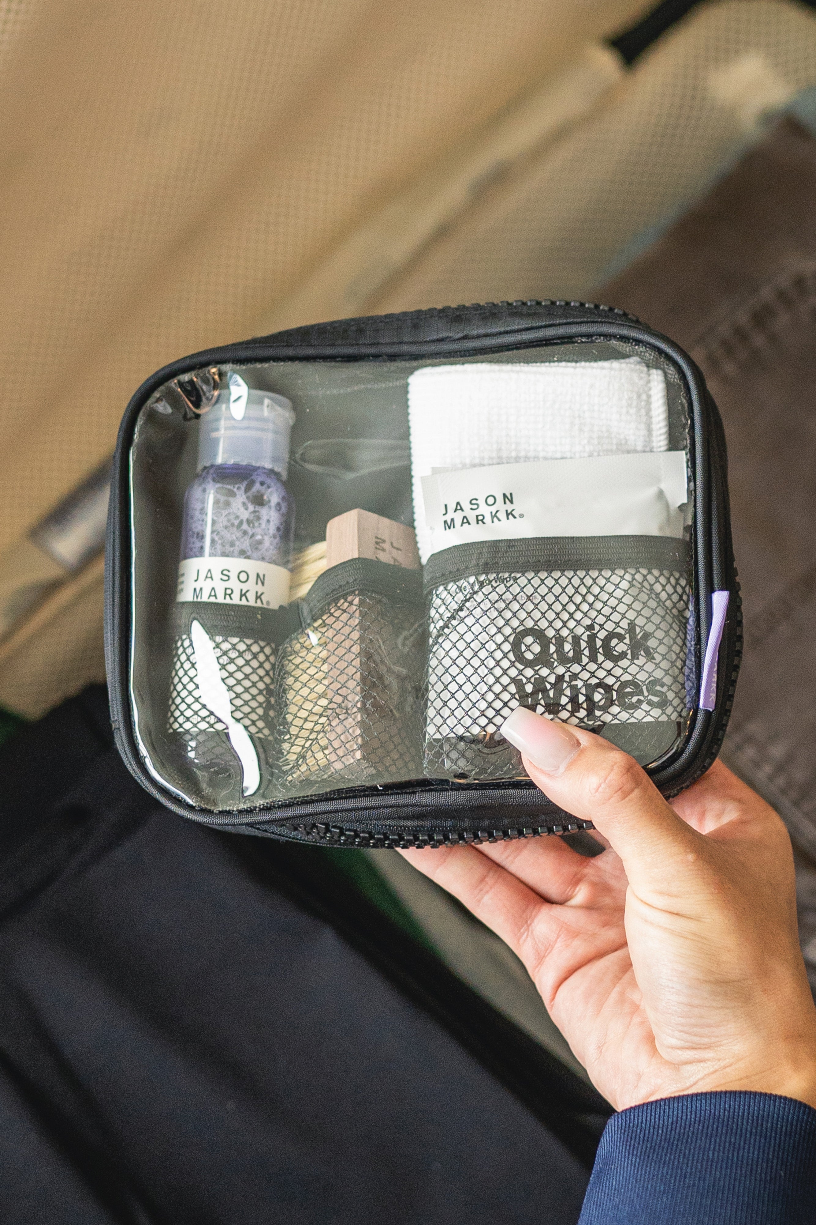 Hand holding a small black travel pouch with cleaning supplies inside, against a blurred background.