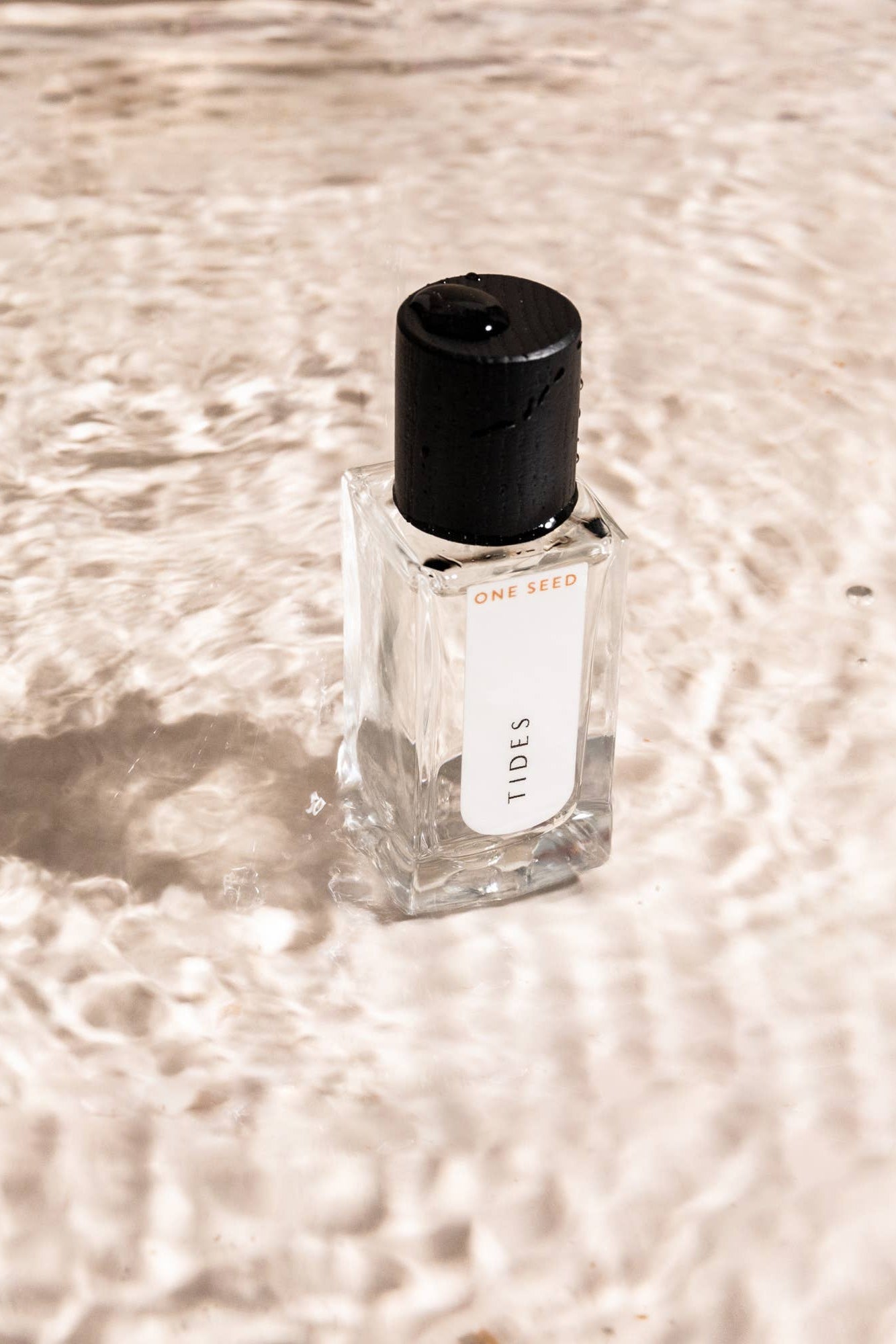 Small fragrance bottle from One Seed labeled 'Tides' on a sandy water surface