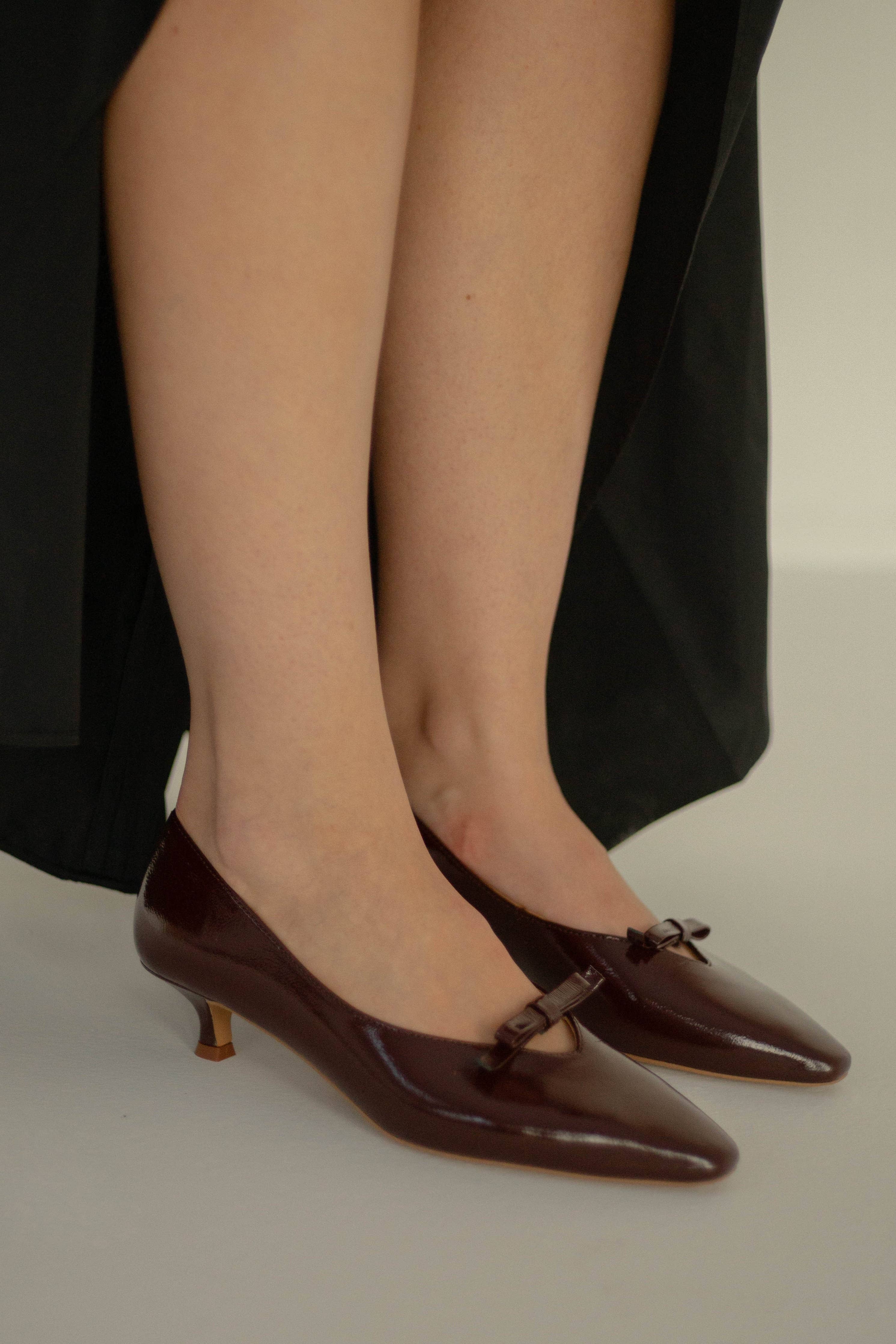 Brown high-heeled shoes worn with a black skirt on a neutral background