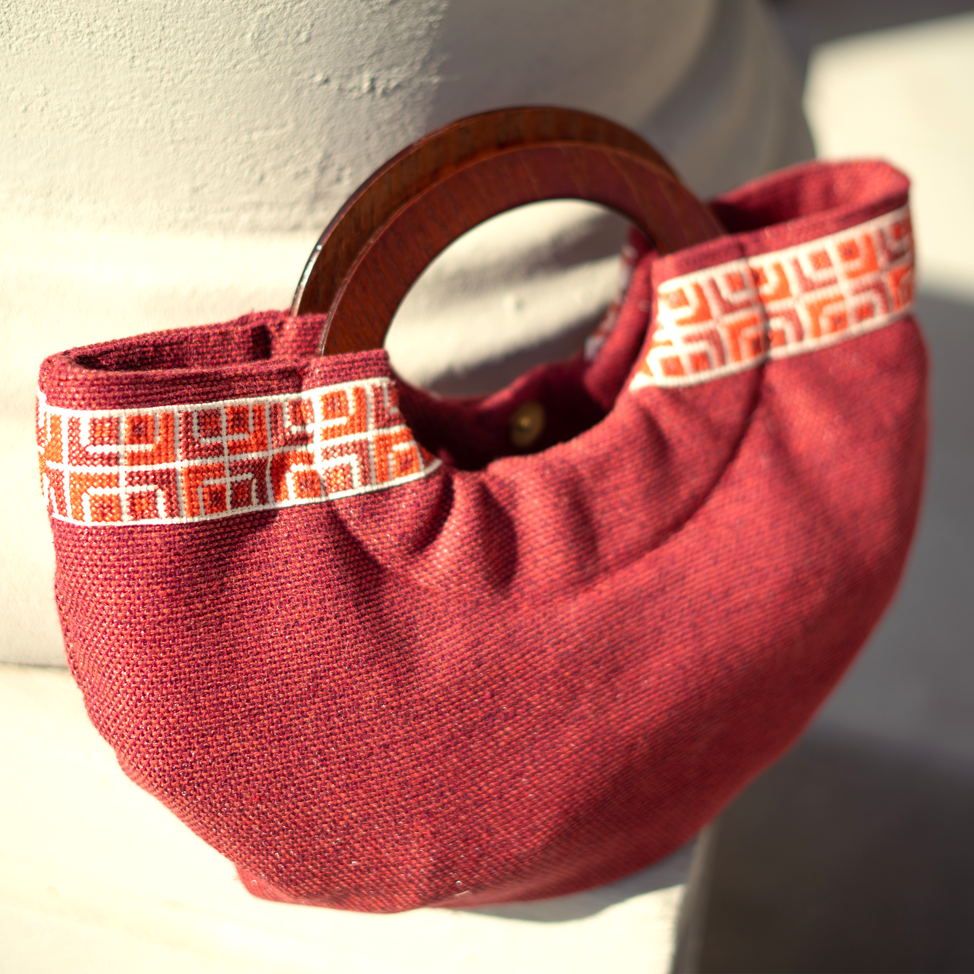 A handmade half moon red clutch with a wooden handle and orange patterned strap.