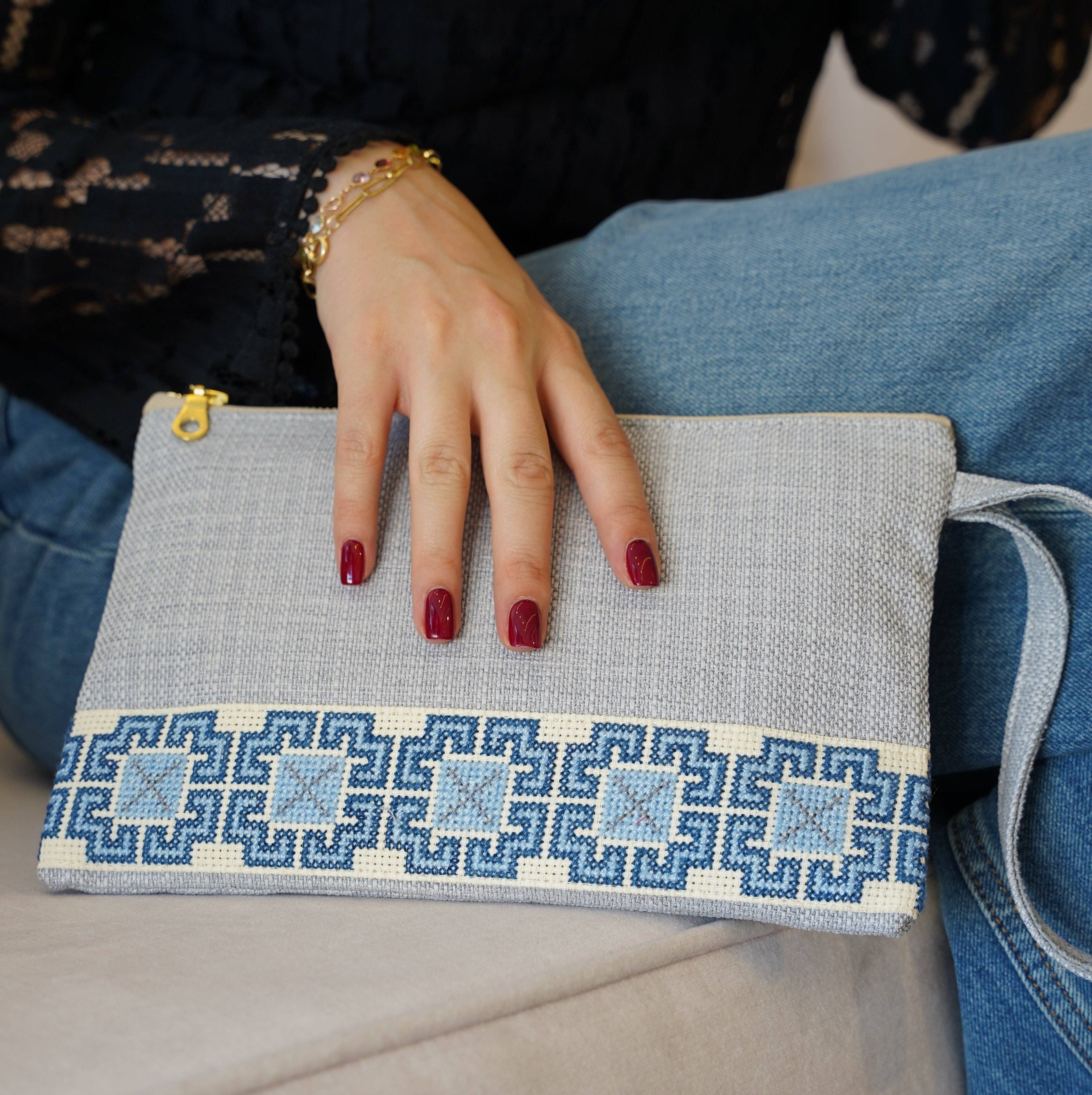 Hand holding a gray clutch with blue geometric pattern, wearing red nail polish.