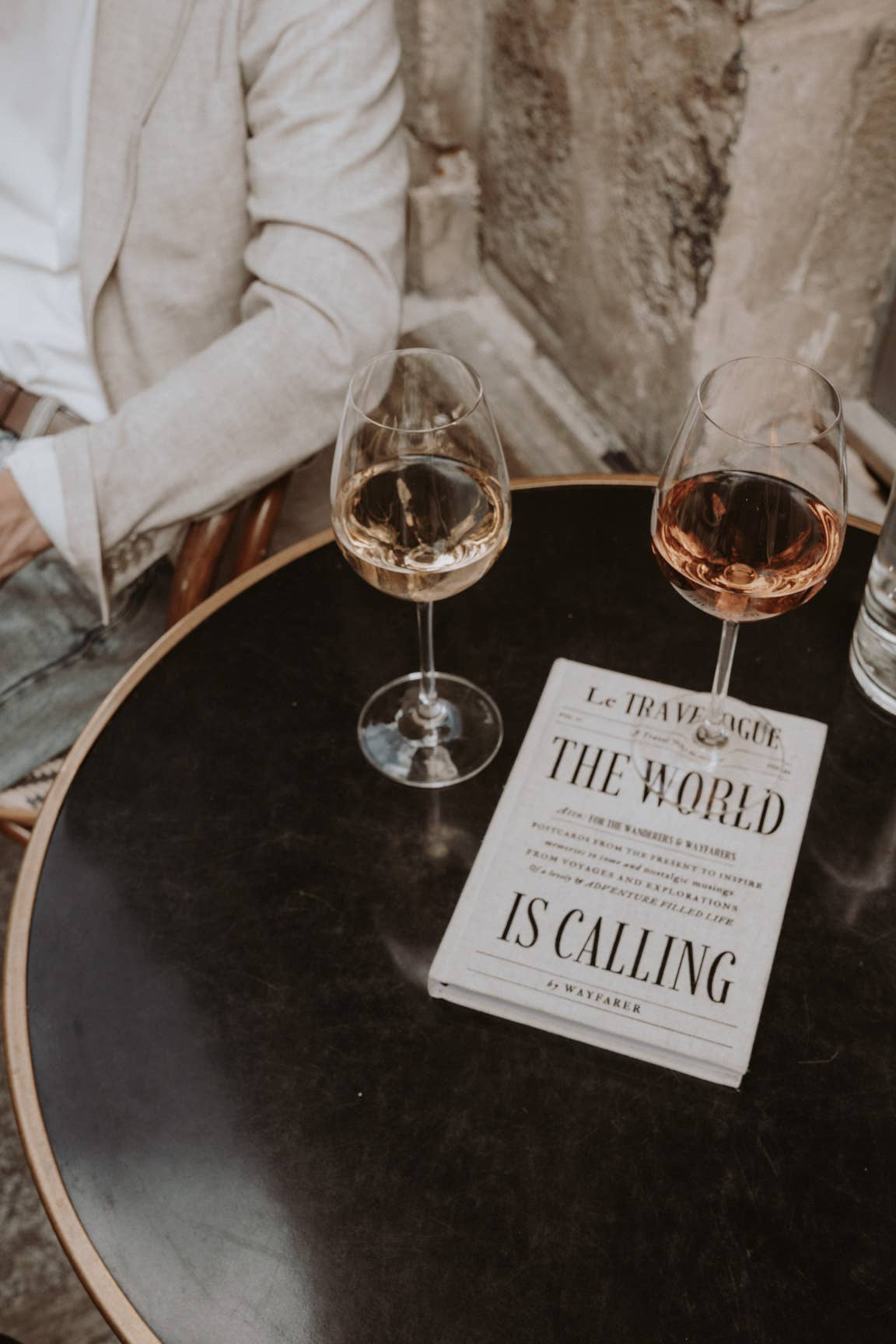 Two wine glasses on a table with a sign reading 'The World is Calling' in an outdoor setting.