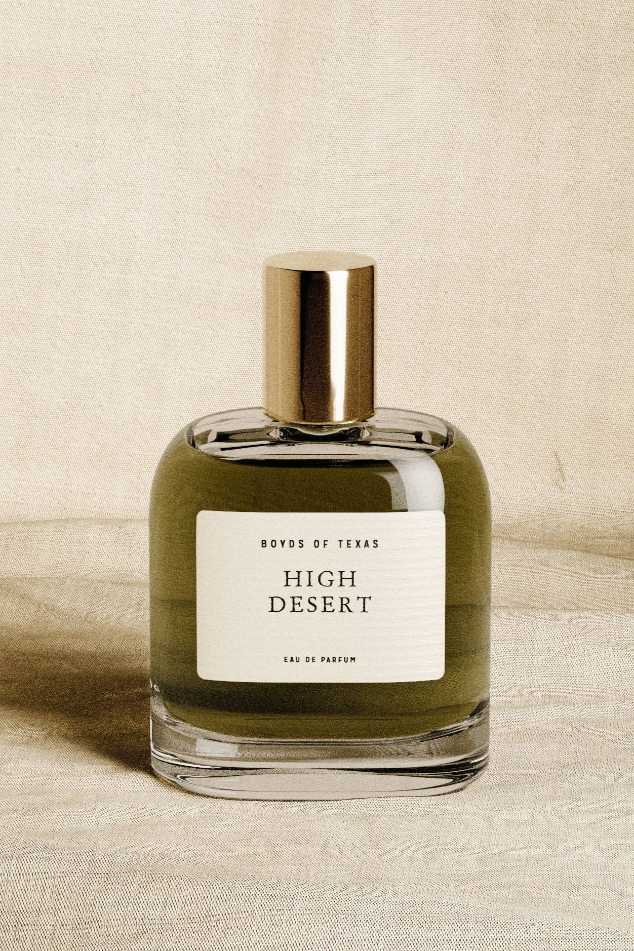 Perfume bottle labeled 'High Desert' by Boys of Texas on a beige fabric background