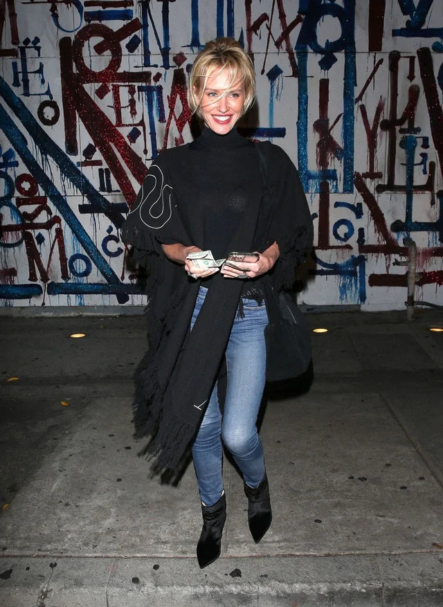 Woman in black poncho and jeans standing in front of a graffiti wall