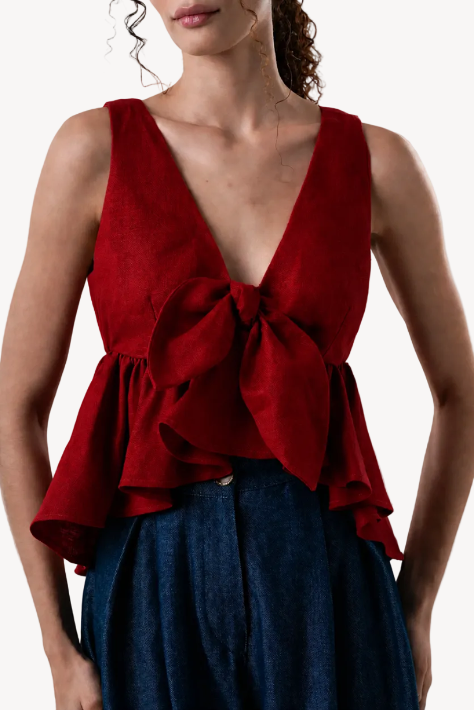 Red sleeveless top with a bow detail worn by a model on a white background