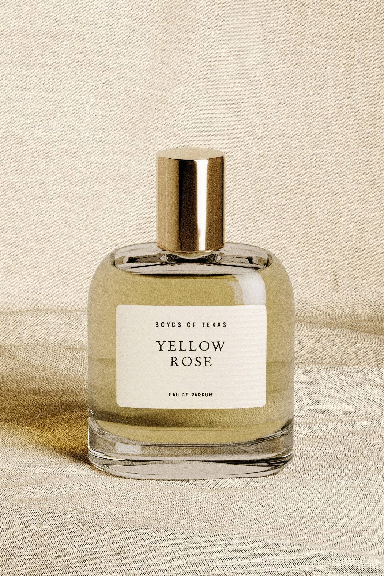 Perfume bottle labeled 'Yellow Rose' by 'Boyds of Texas' on a beige fabric background
