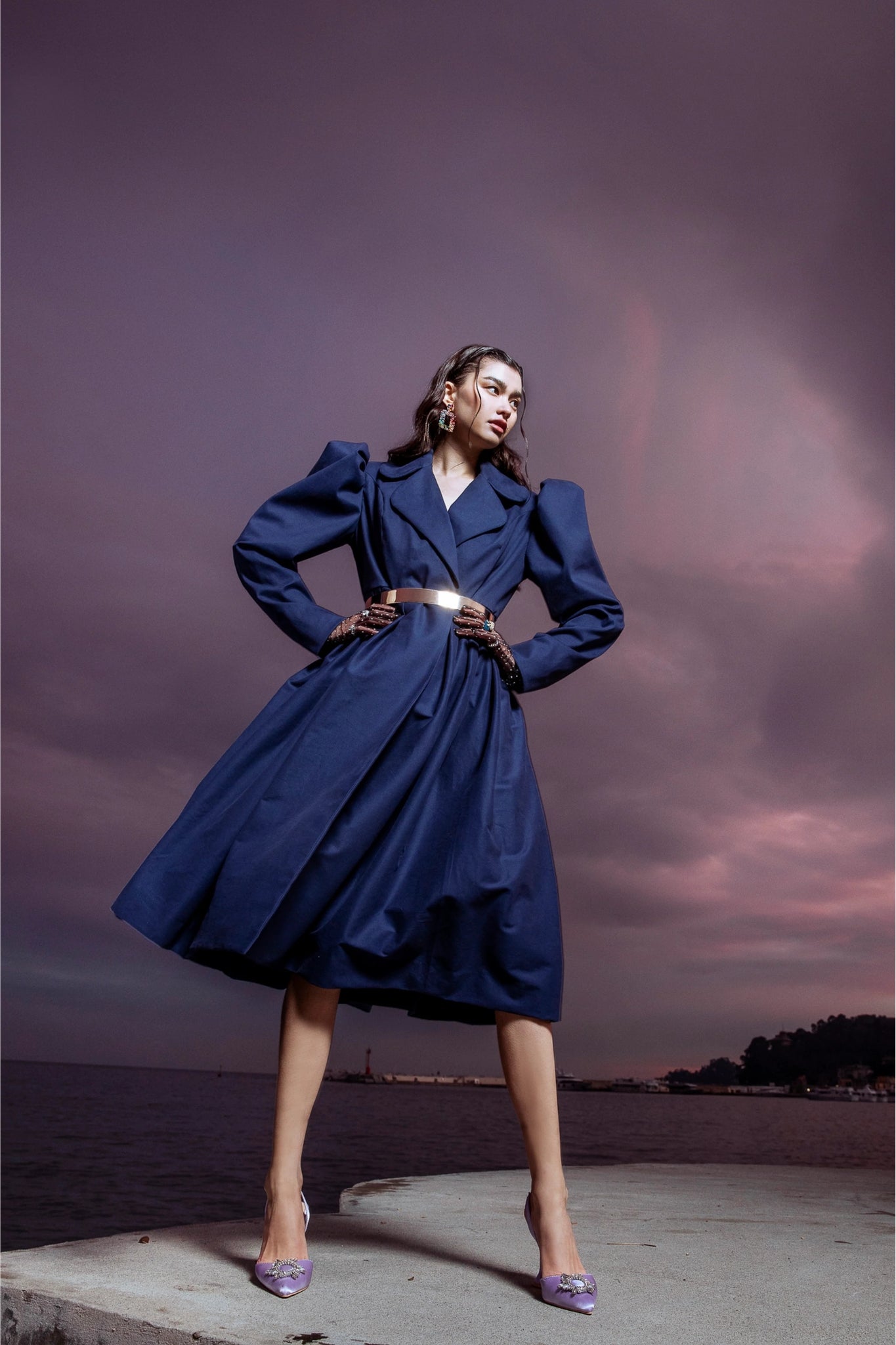 Woman in a blue coat standing on a dock with a purple sky background