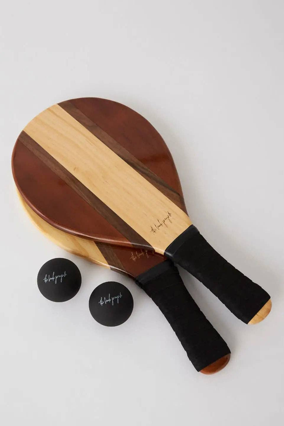Wooden paddle with black handles and two balls on a light gray background