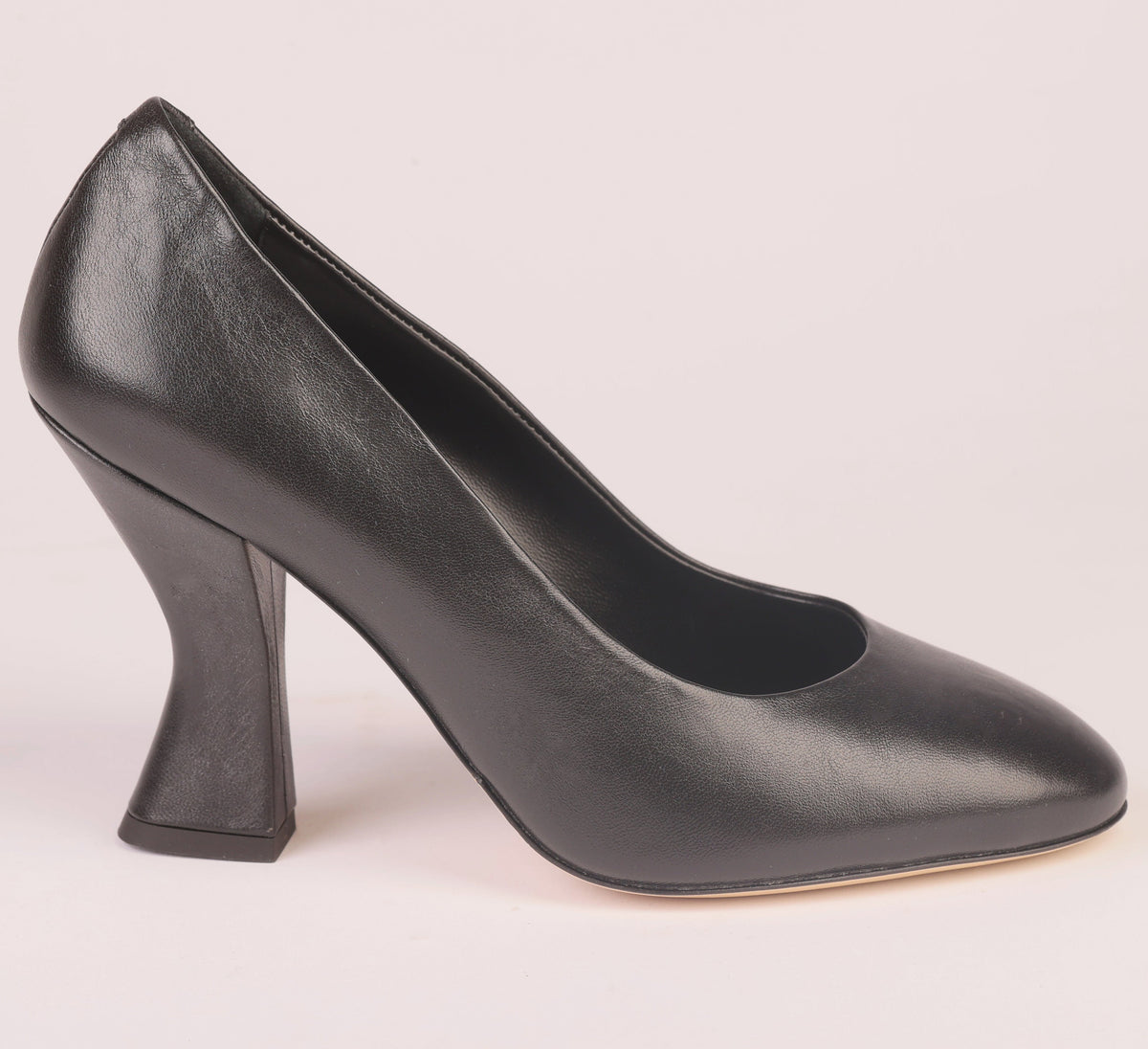 A single black leather high-heeled pump with a pointed toe and sculptural block heel, shown in profile against a light pink background.