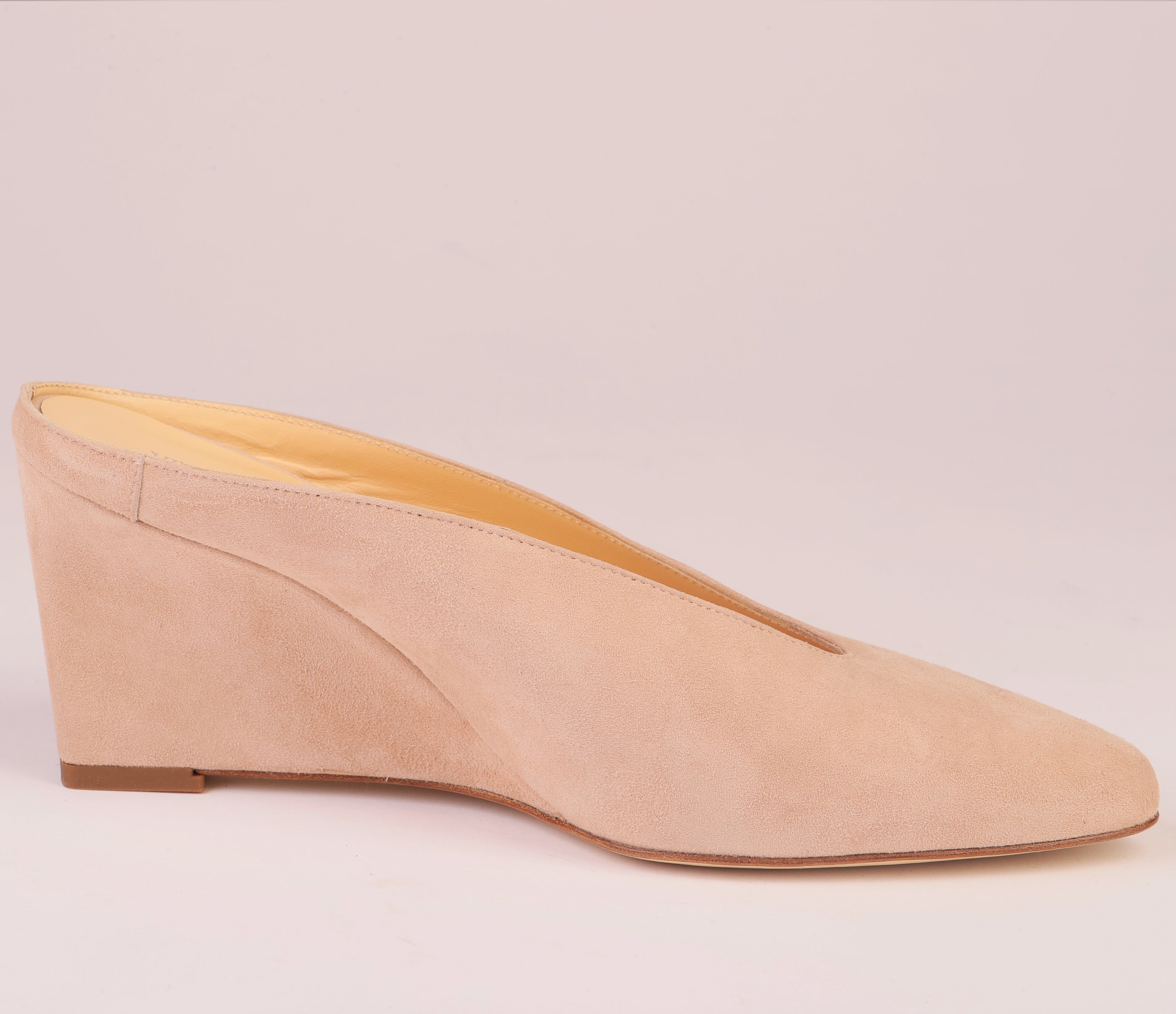 A single nude beige suede wedge mule shoe with a pointed toe, shown in profile against a solid pale pink background.
