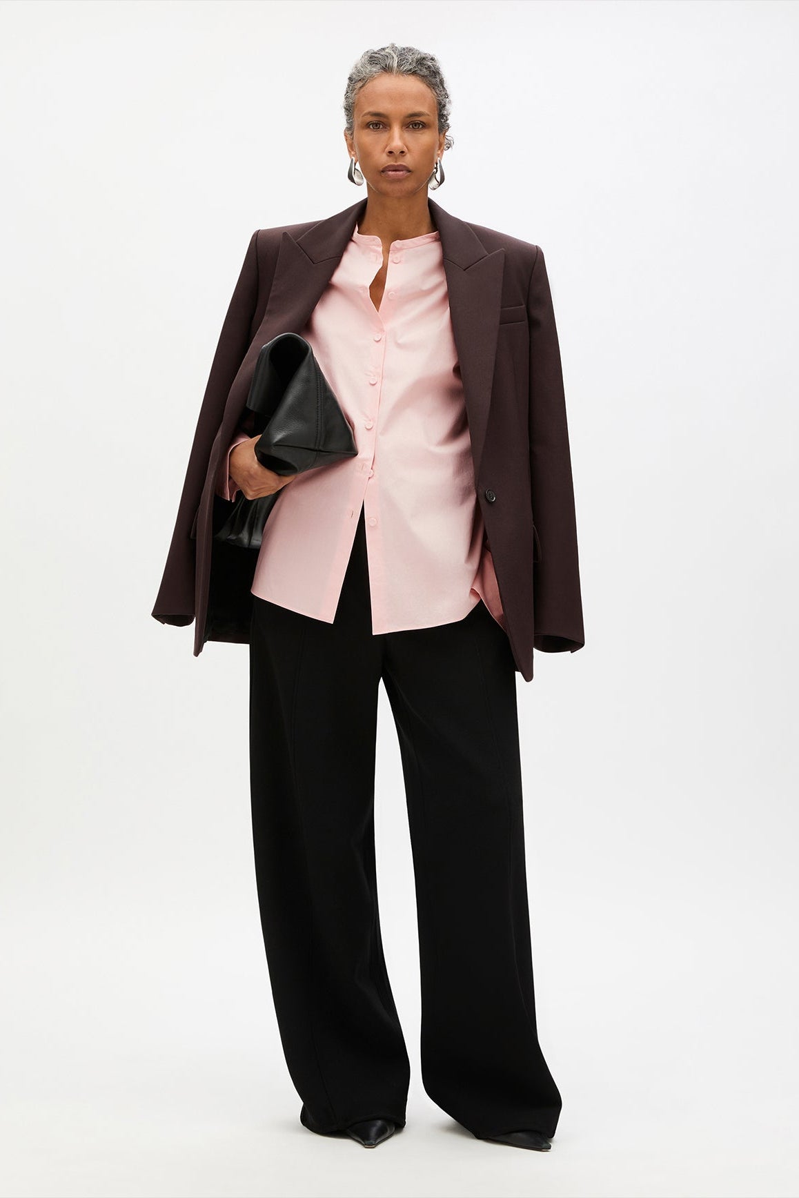 Woman wearing a brown blazer, pink blouse, and black pants on a white background